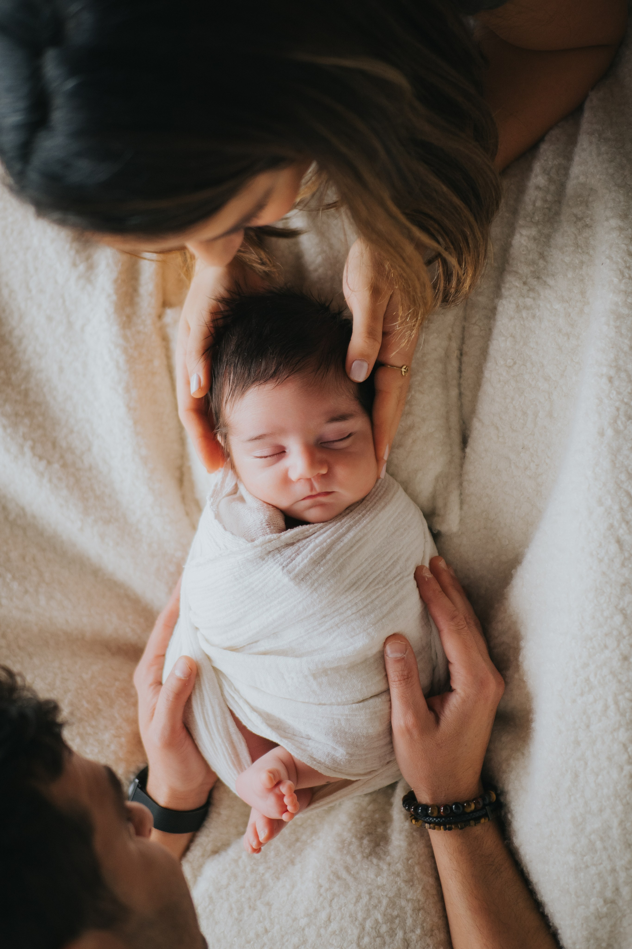 Séance nouveau-né en lumière naturelle avec emmaillotage blanc et mains des parents, Mimosa Studios Montréal.
