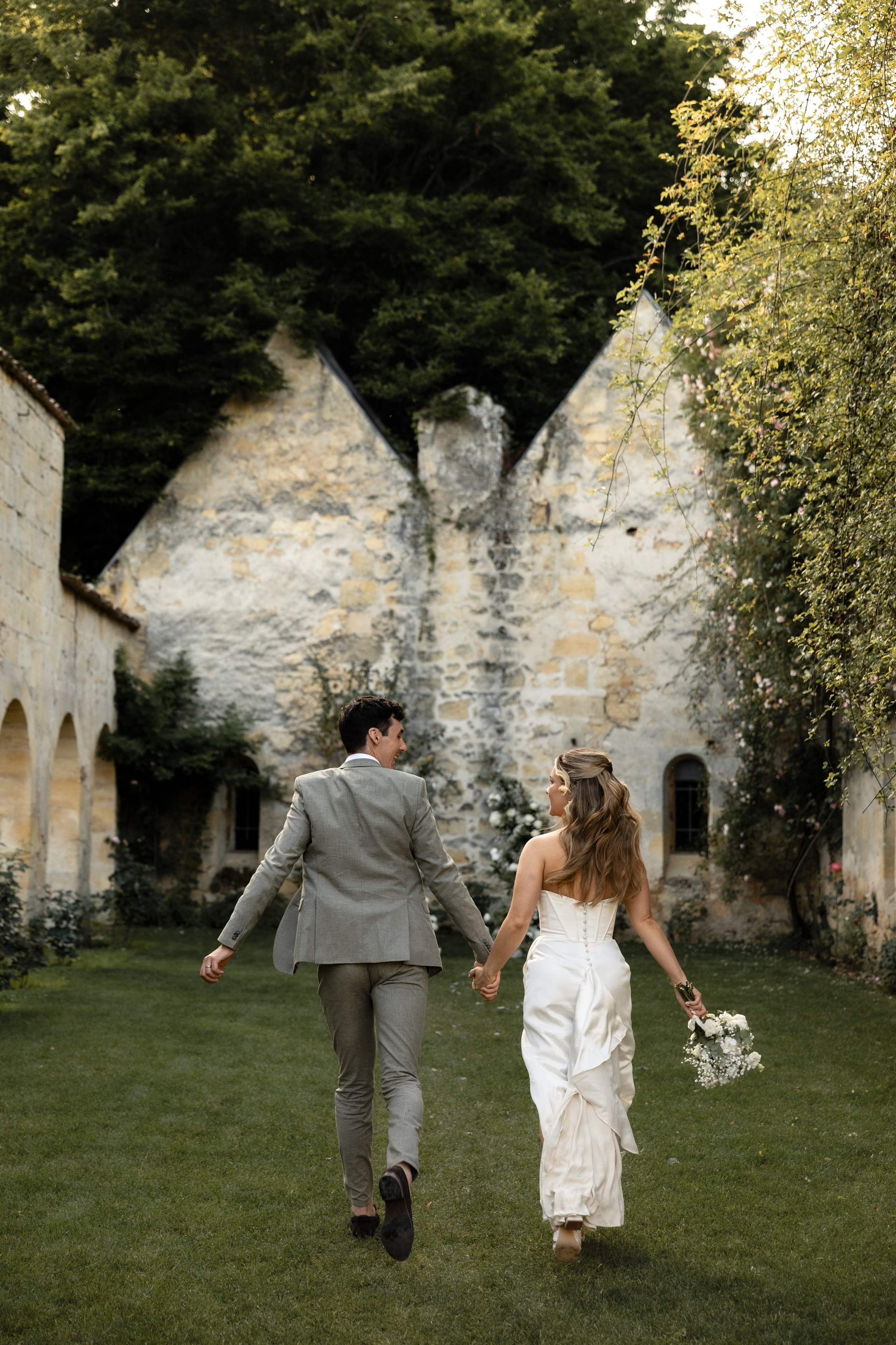 Bride and groom walking hand in hand through the historic garden of Château Sentout during their destination wedding in France.