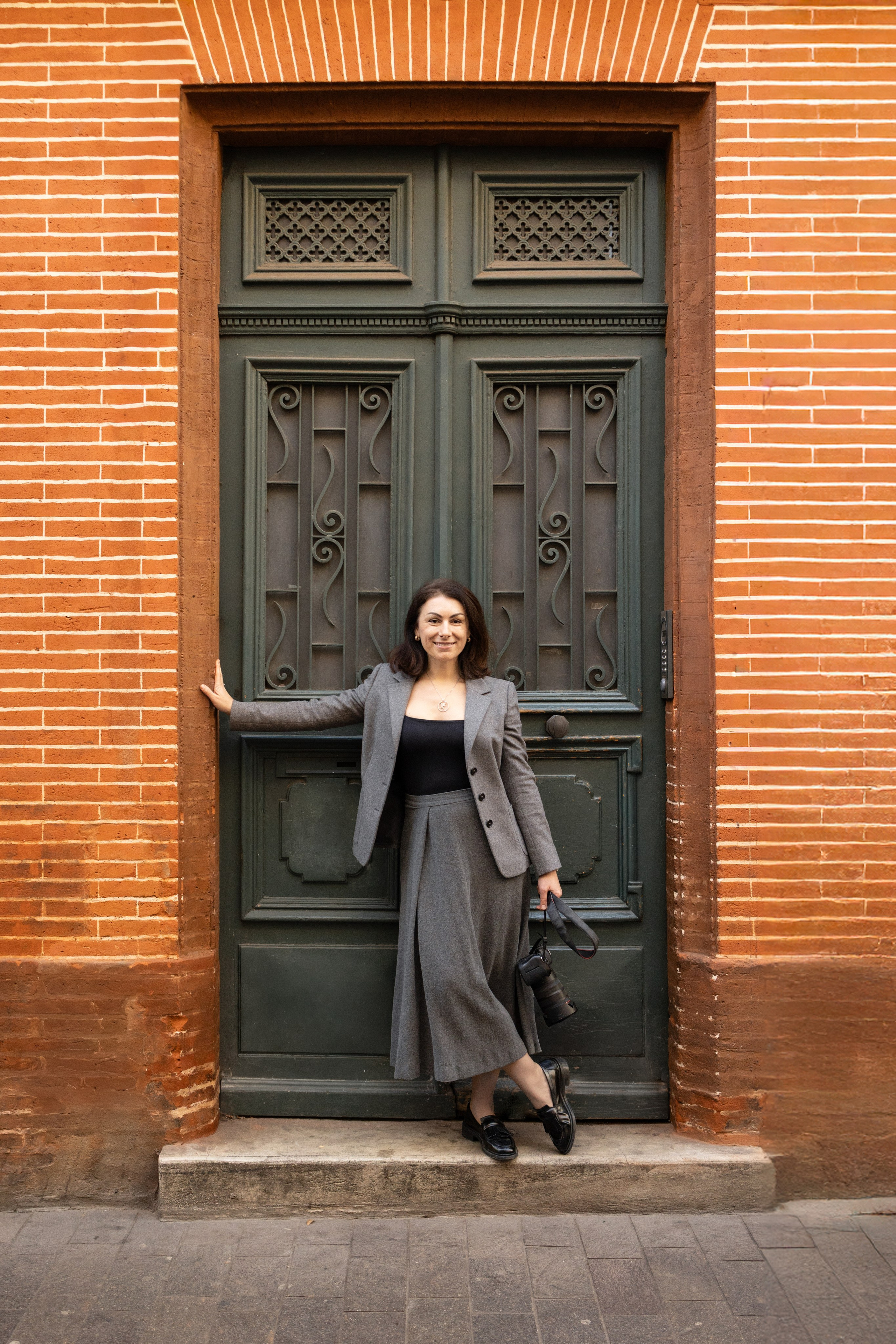 Personal branding portrait of a corporate photographer in Toulouse, in professional attire, in front of a brick door, natural light