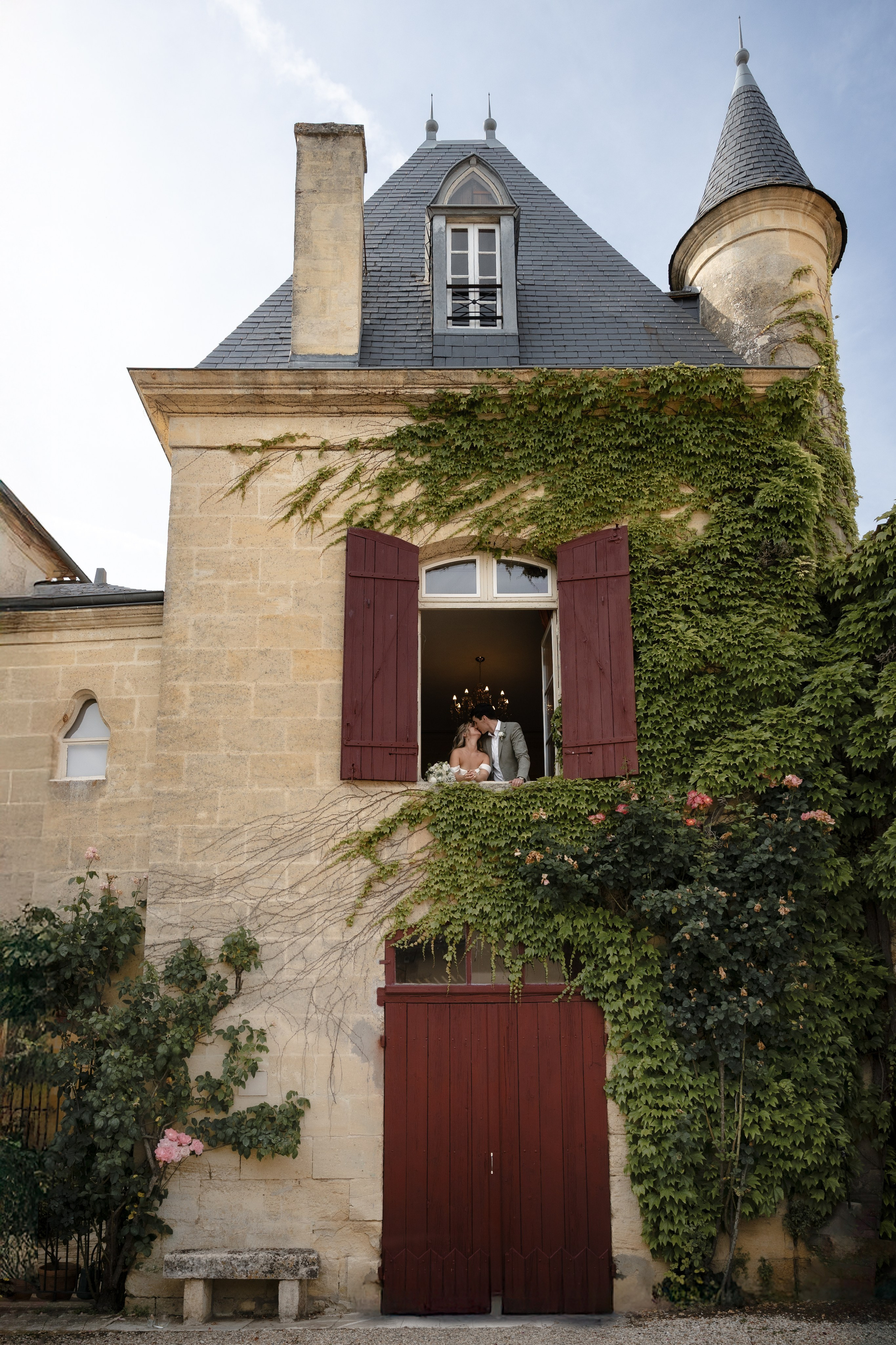 Bride and groom sharing a kiss in the window of Château Sentout surrounded by ivy during their wedding in Southwest France.