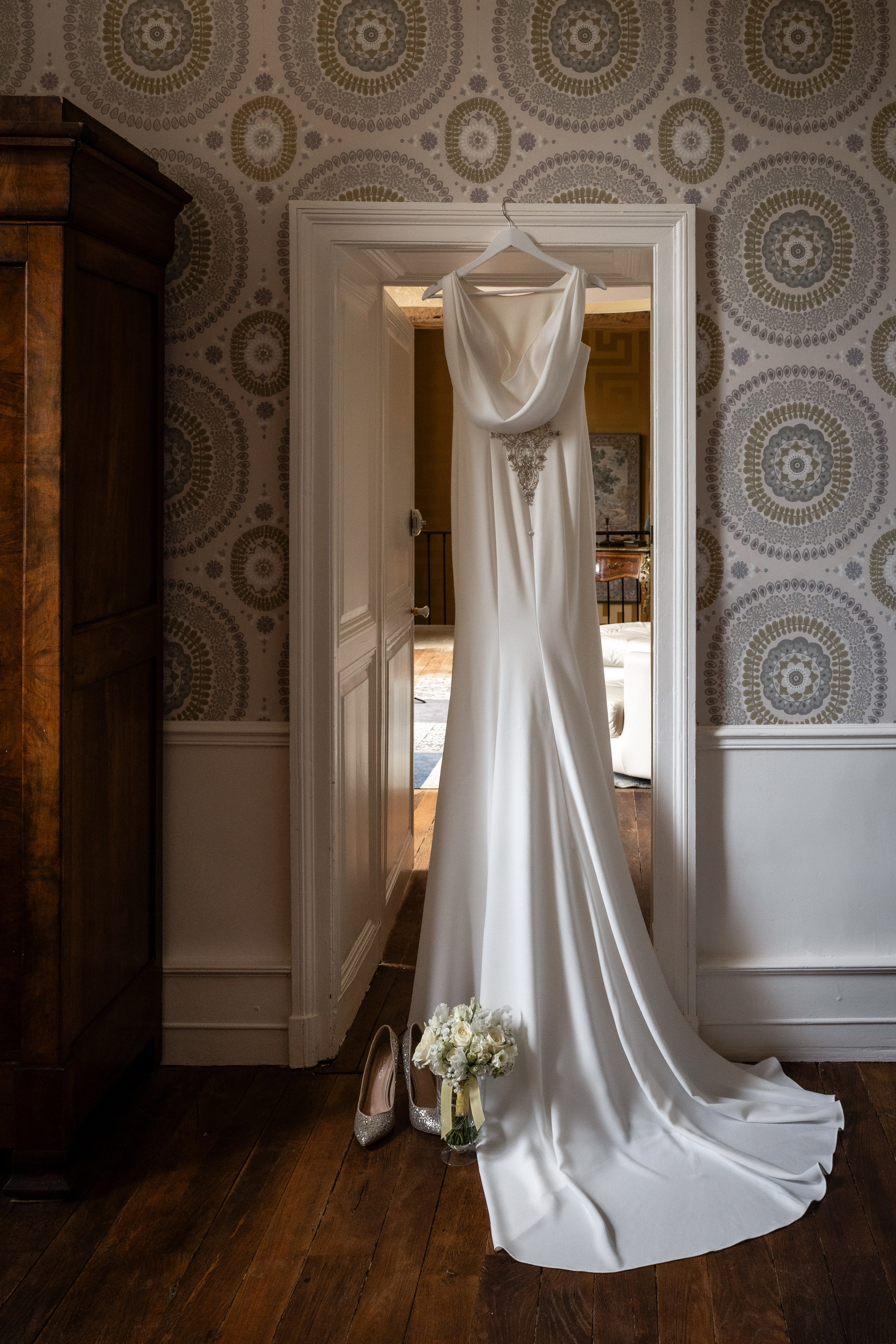 Wedding dress with a long train hanging in a doorway against patterned wallpaper