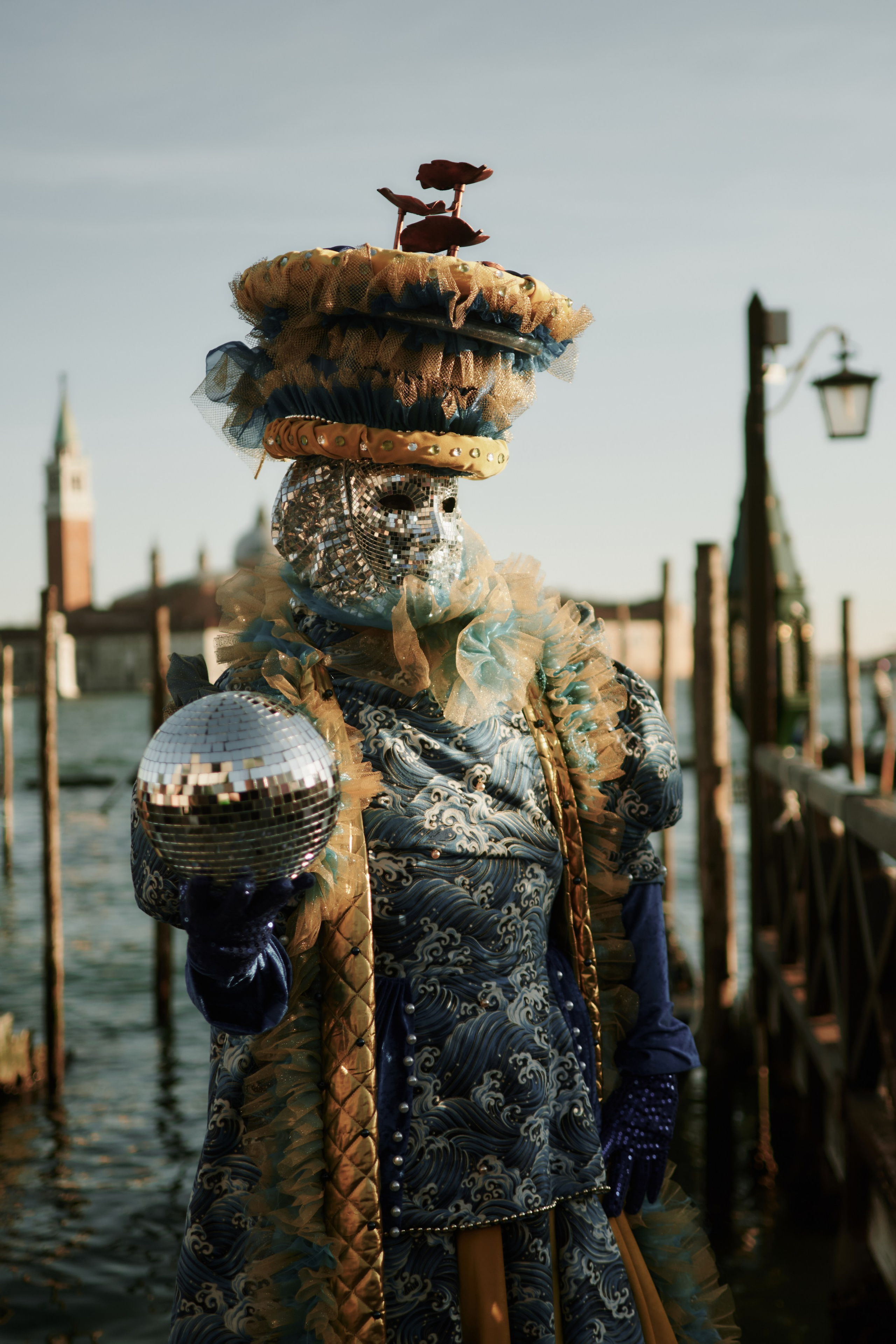 A close-up of a Venetian carnival mask with intricate details and feathers. A man wearing a traditional Venetian costume and mask holding a cane and posing for a portrait.