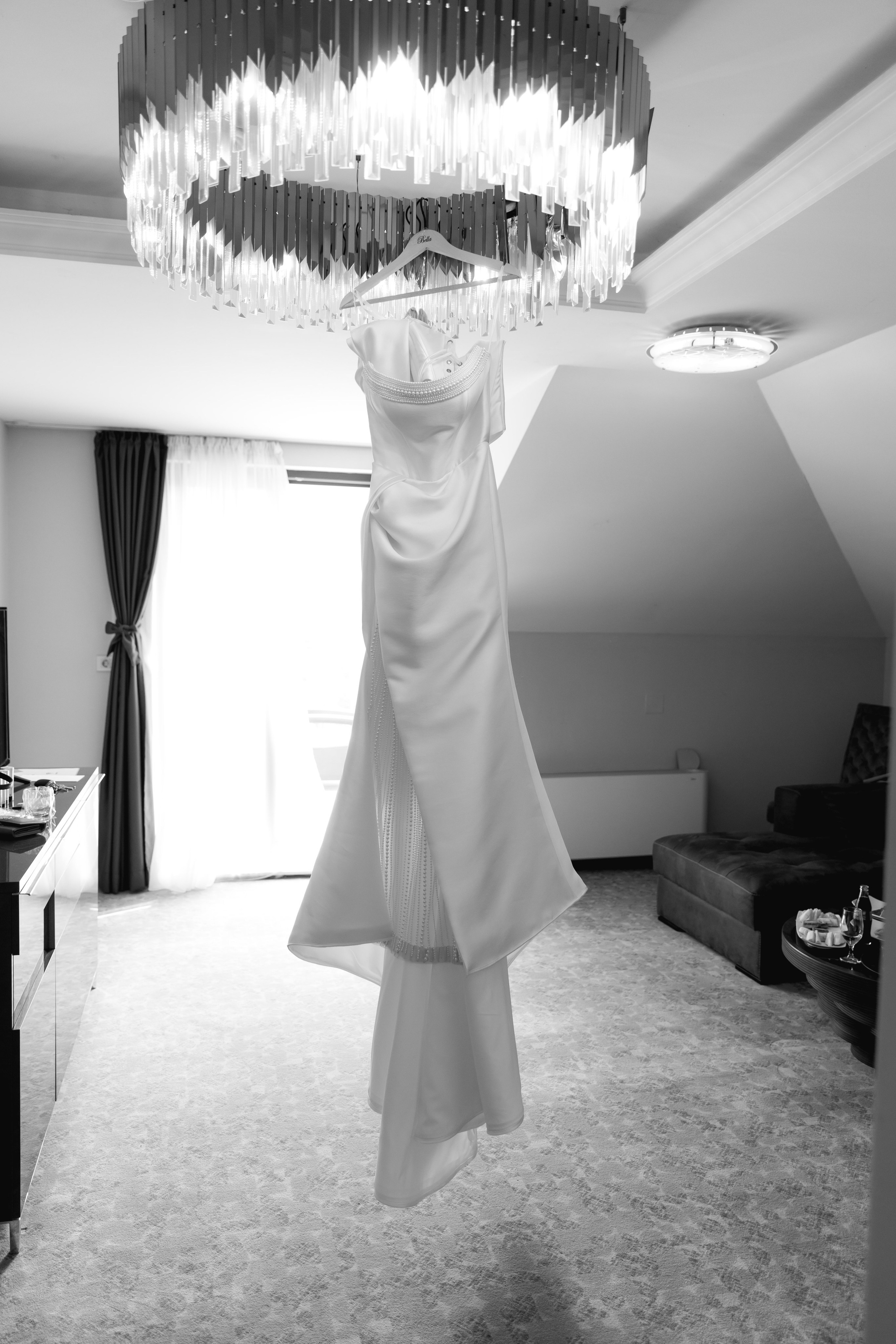 Elegant wedding dress hanging in a hotel room during bridal preparations, capturing a timeless wedding detail before the ceremony.