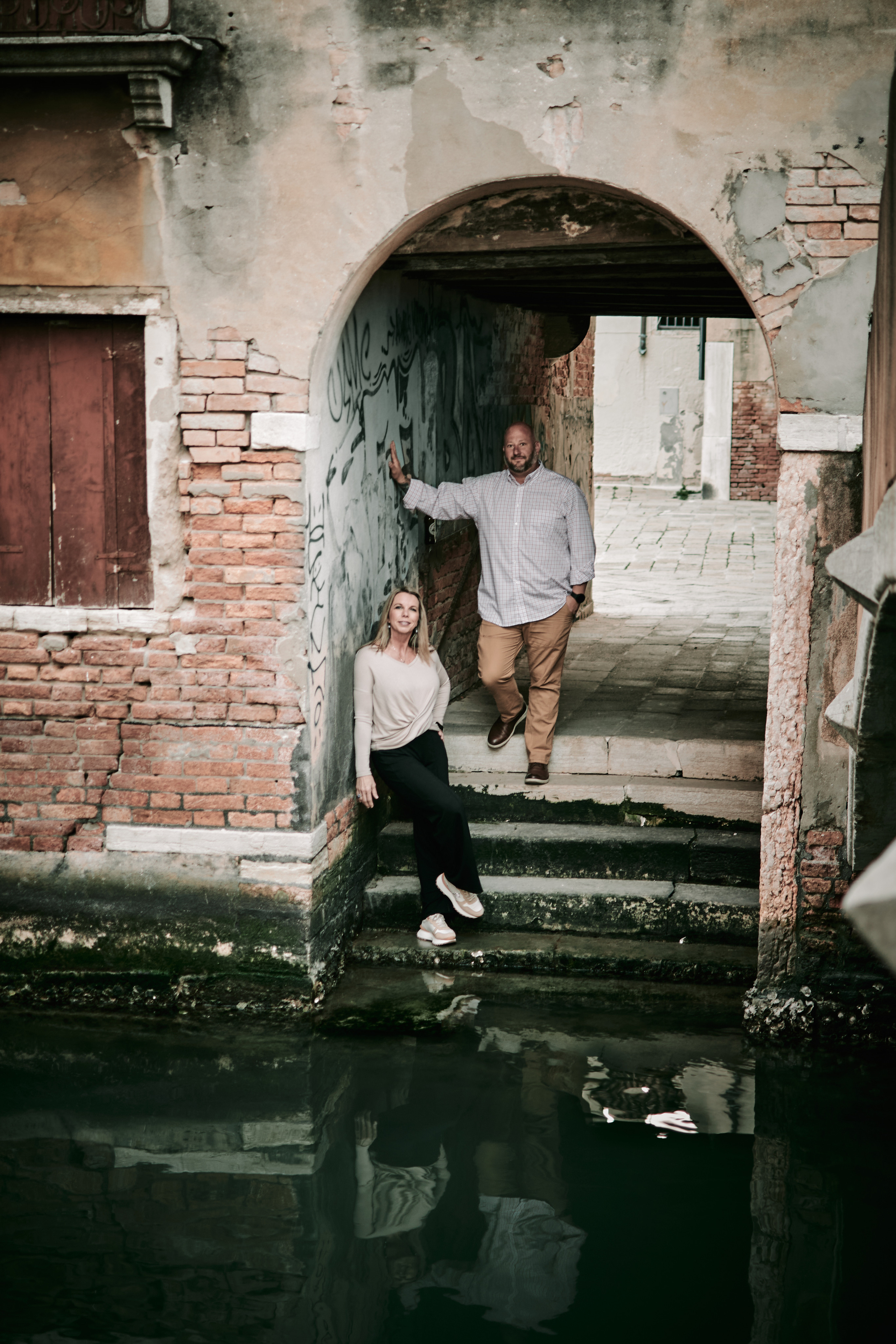 A couple embraces on a Venetian bridge with the city's iconic canals and architecture in the background
