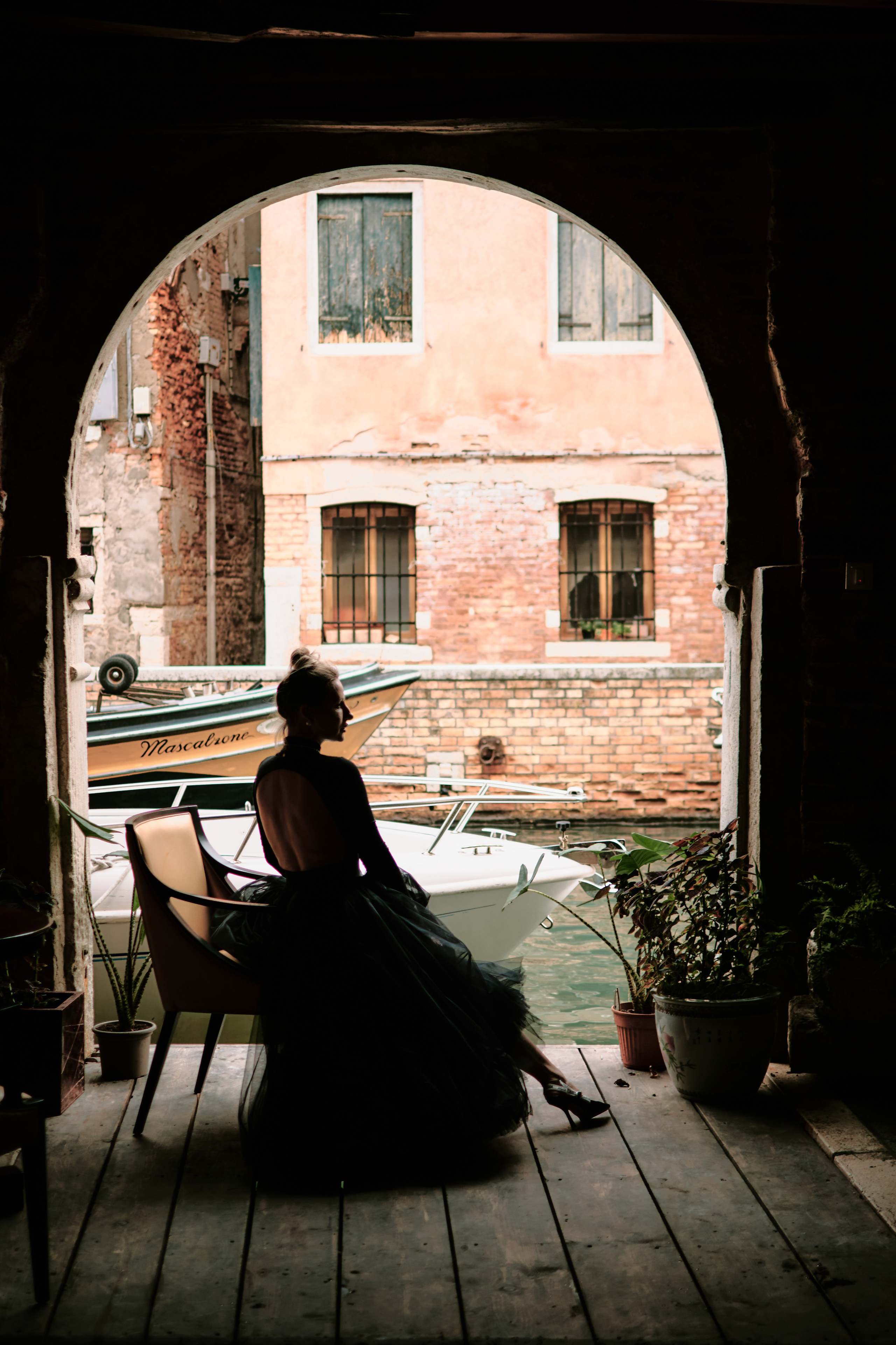 A stunning young woman in a black dress stands in San Marco Square, Venice, with the historic Arca di San Marco in the background. The architectural details of the Arca and the surrounding buildings add to the romantic atmosphere of the scene. The woman's dress drapes elegantly around her figure, adding to the captivating allure of the photo. The contrast between the dark dress and the warm colors of the surrounding buildings adds to the overall visual impact of the image, creating a sense of mystery and intrigue