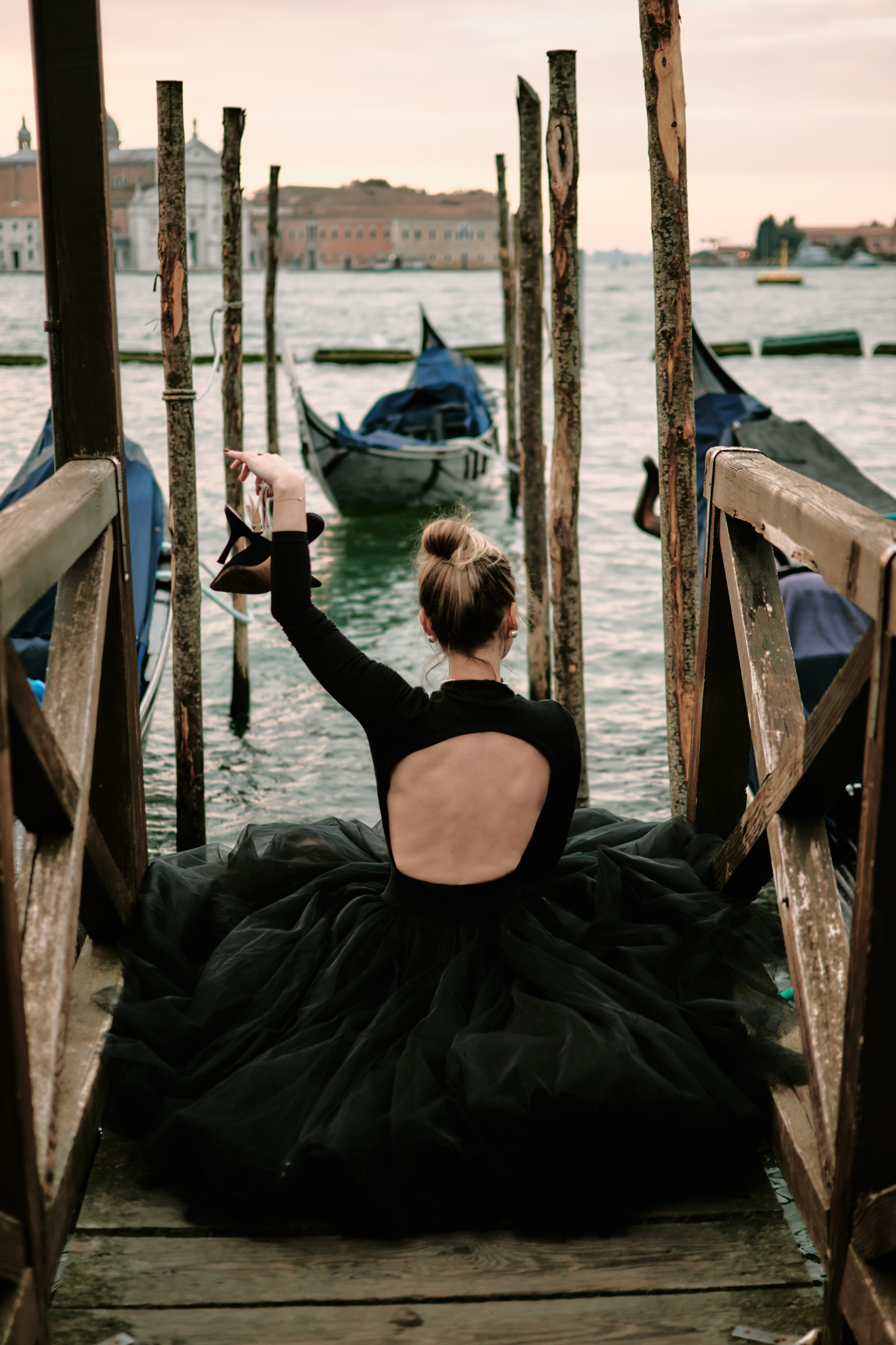 A woman stands in the heart of San Marco Square in Venice, wearing a stunning black dress that accentuates her beauty. The panoramic view of the Laguna in the background adds to the romantic atmosphere of the scene. The ornate architecture of the surrounding buildings is a testament to the city's rich history and culture. The woman's hair flows gently in the breeze as she gazes out at the stunning view, lost in thought. The vibrant energy of the bustling square is palpable, making for a truly memorable photo shoot. Fashion blogger shoot Venice. Portrait and Fashion Photographer in Venice, Italy. Instagram Photos with lifestyle photographer