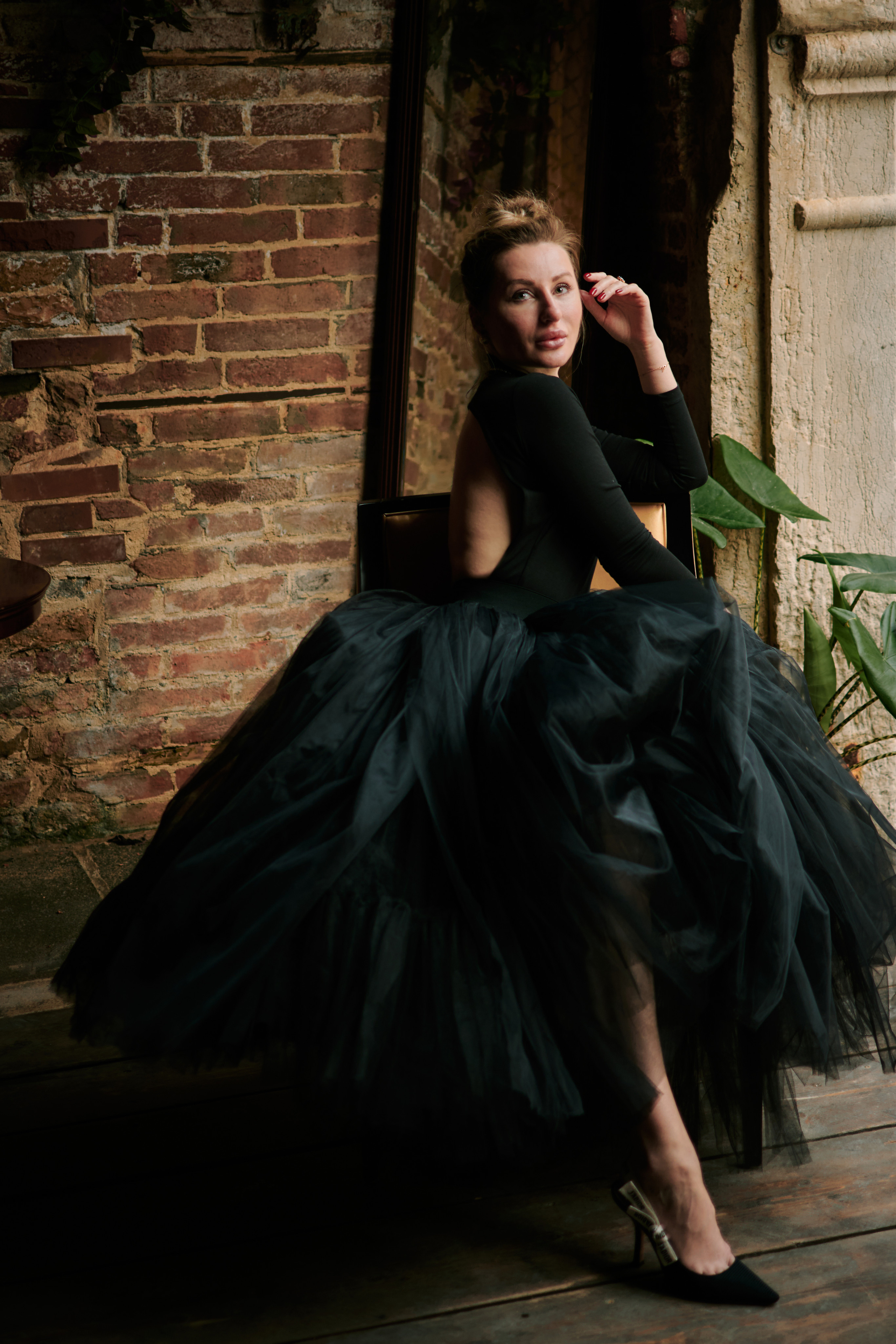 A captivating young woman in a flowing black dress stands on a narrow bridge, framed by the intricate stonework of the arches above her. The scene is full of mystery and romance, with the gentle canal waters below and the timeless beauty of Venice's architecture surrounding her.