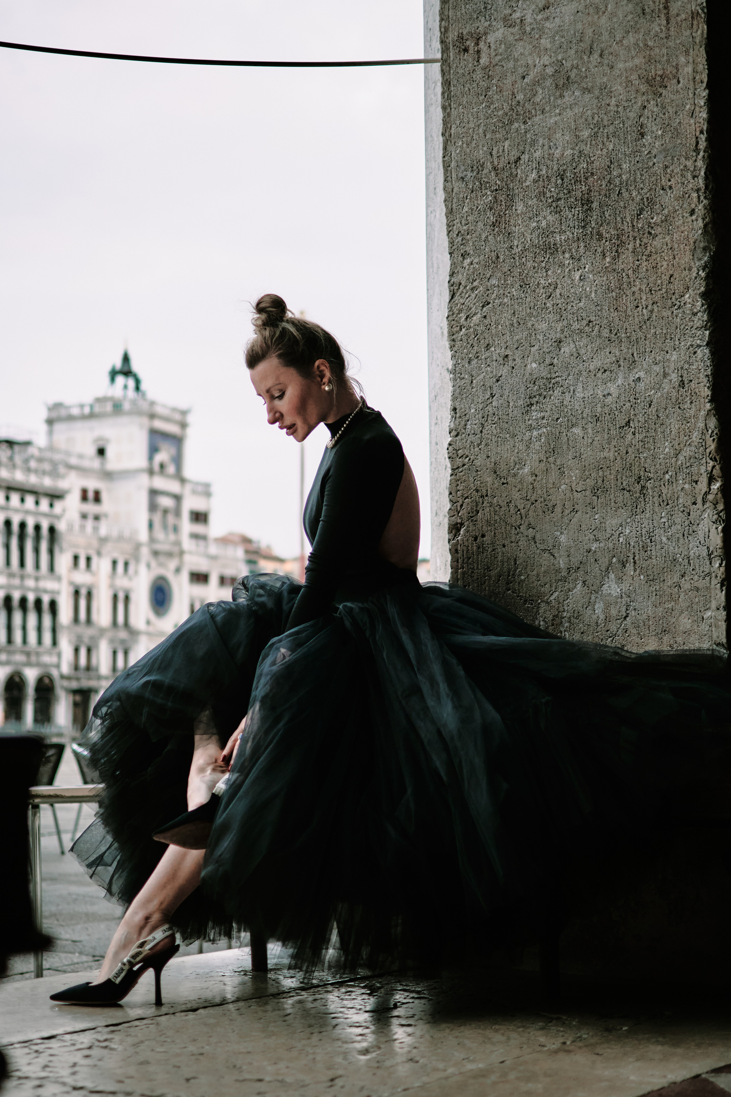 A young woman stands on San Marco Square, gazing at the stunning architecture and bustling crowds around her. The sun casts a warm glow on her face, highlighting her delicate features and soft, flowing hair. She wears a flowing dress that seems to dance in the breeze, accentuating her graceful movements. The intricate details of the nearby buildings and the vibrant colors of the street performers create a romantic and captivating atmosphere around her, making for a beautiful and memorable portrait.