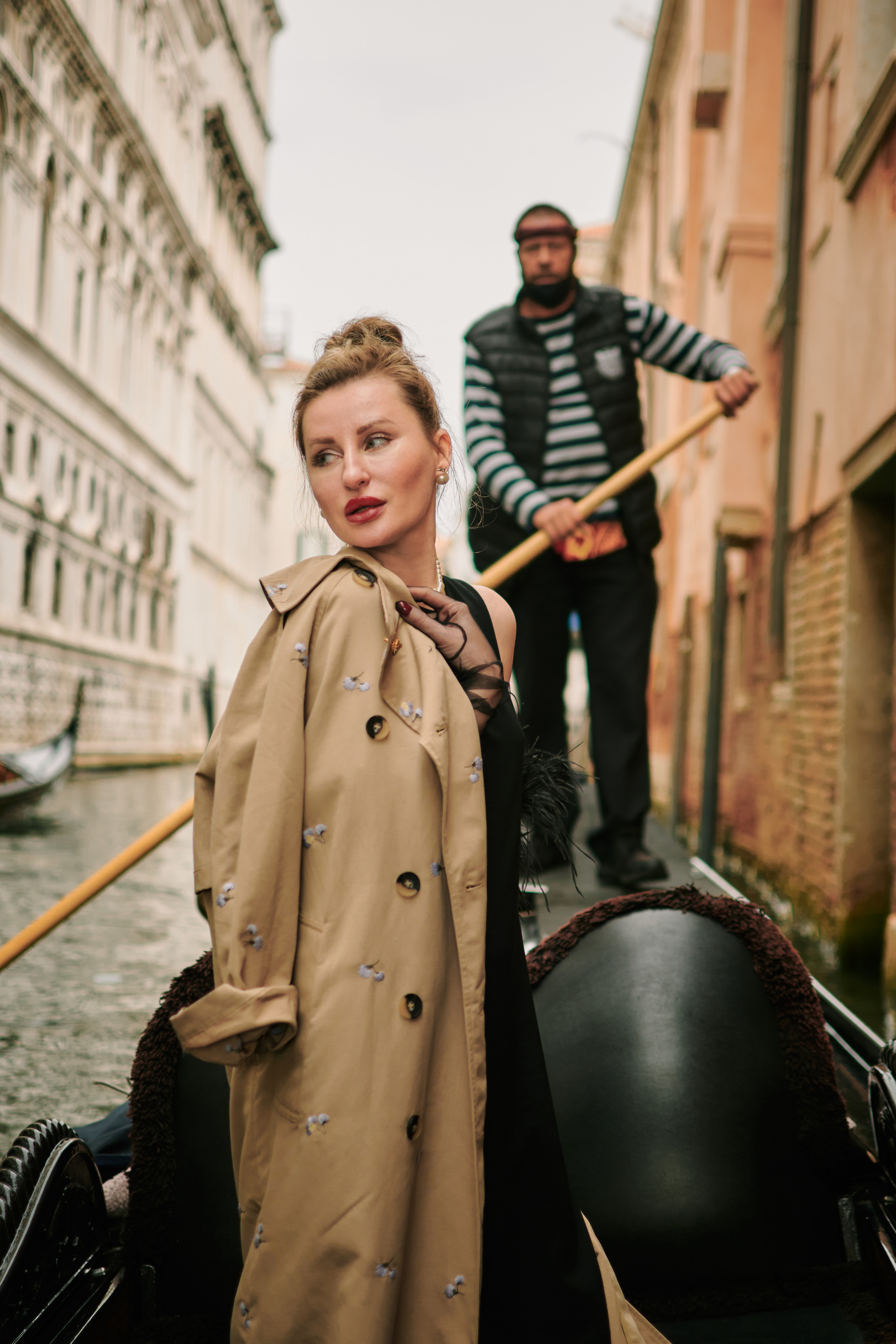 A young woman is enjoying a gondola ride on a canal in Venice. The gondolier is steering the boat while the family takes in the beautiful scenery, including the colorful buildings and bridges that line the waterway.