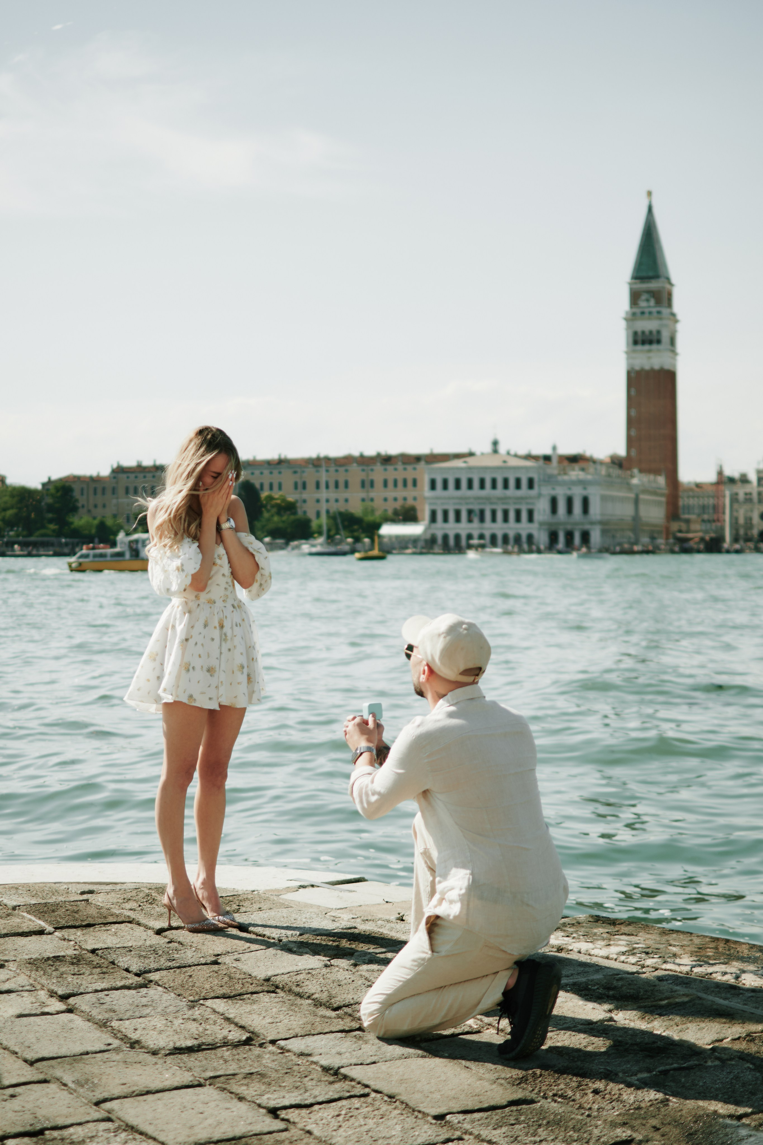 boy and girl love story in san marco square in venice.A couple stands hand in hand on a narrow cobblestone street in Venice. The winding alleyway is illuminated by the warm glow of street lamps and the occasional light from a nearby shop window. The couple is dressed in stylish attire, the man in a sharp suit and the woman in a flowing gown. They gaze lovingly into each other's eyes, lost in their own world amidst the charm and romance of the ancient Italian city. In the background, the muted sounds of Venetian life can be heard, adding to the atmosphere of peacefulness and intimacy.