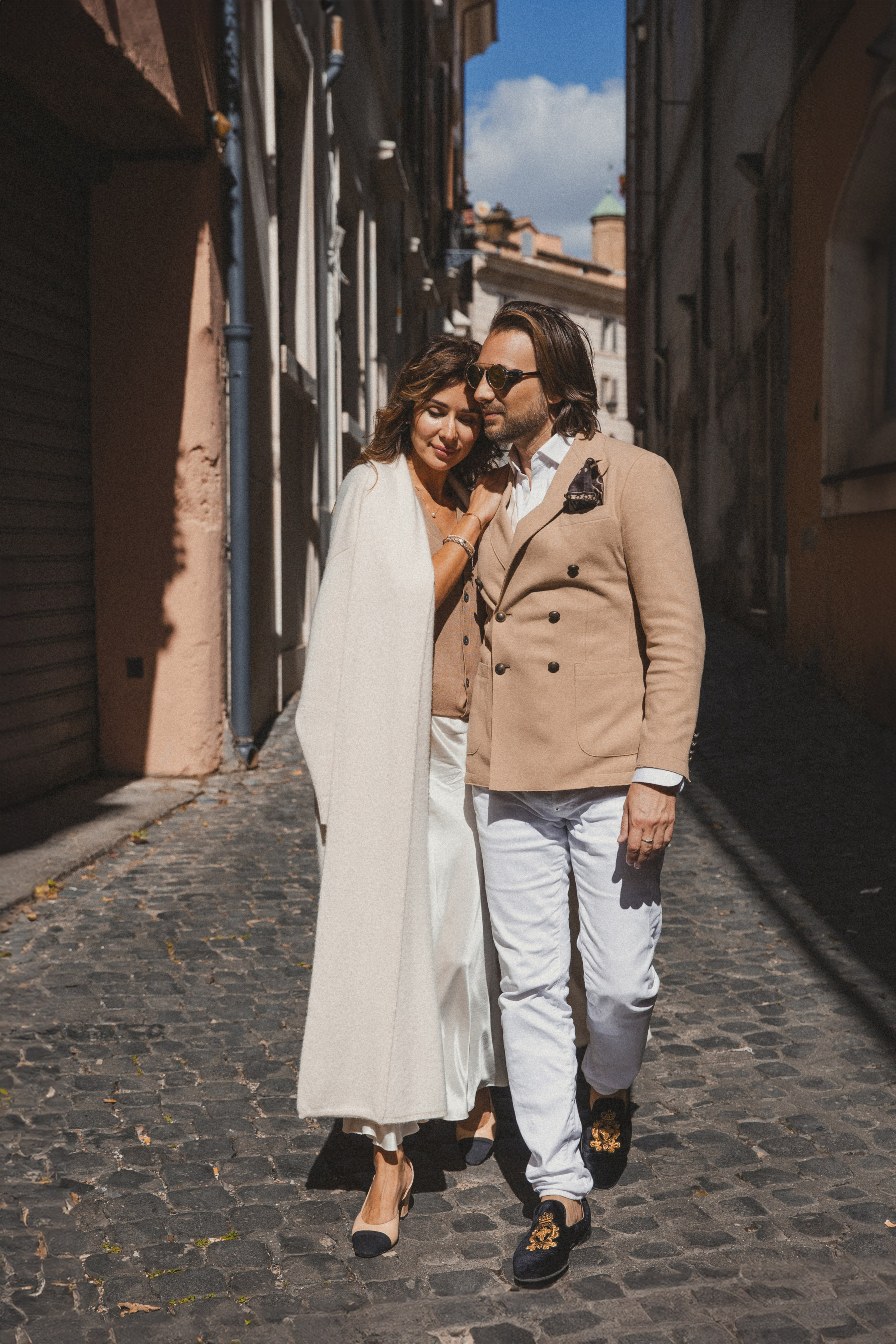 A couple elegantly dressed, walking through the cobbled streets of Rome, hand in hand.