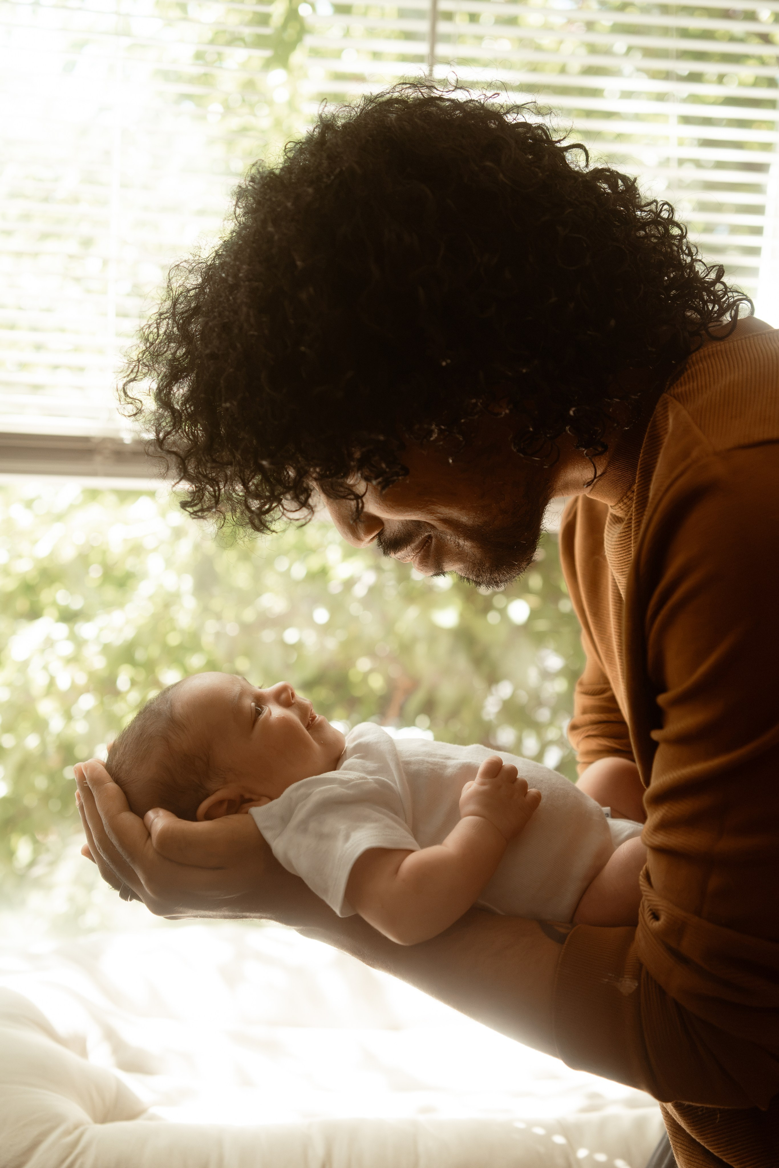 Father holding his newborn in the light of a window at home during a lifestyle newborn session