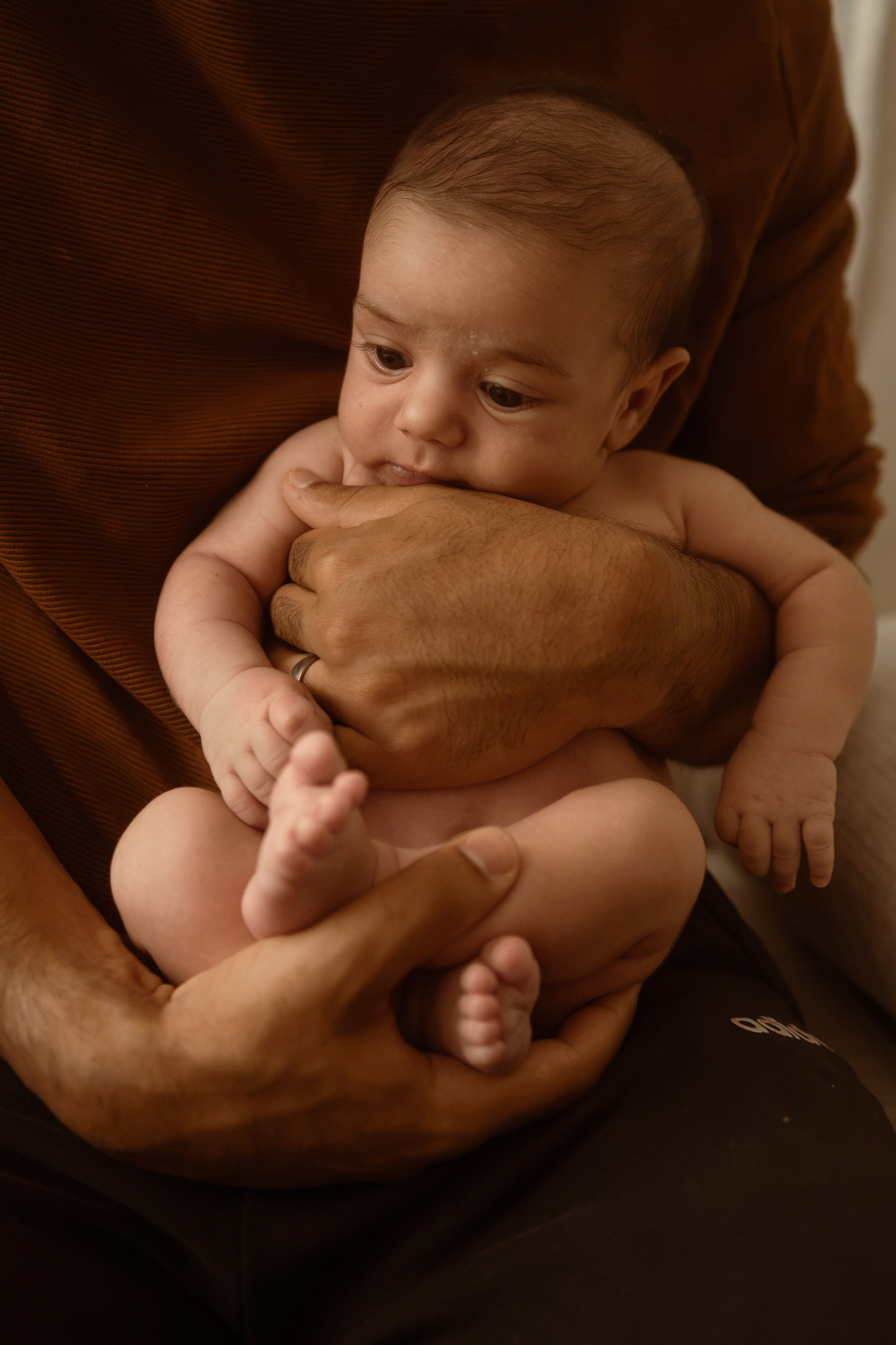 Baby held upright against a parent's chest in a dark studio portrait by a Connecticut newborn photographer