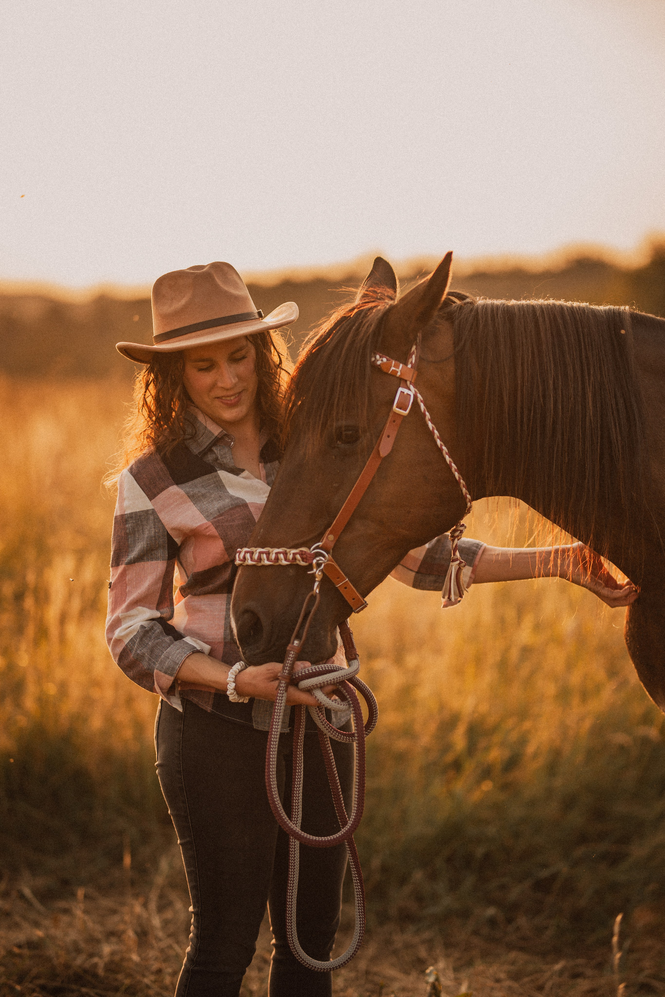 Cowgirl au couché de soleil avec son cheval dans un champ