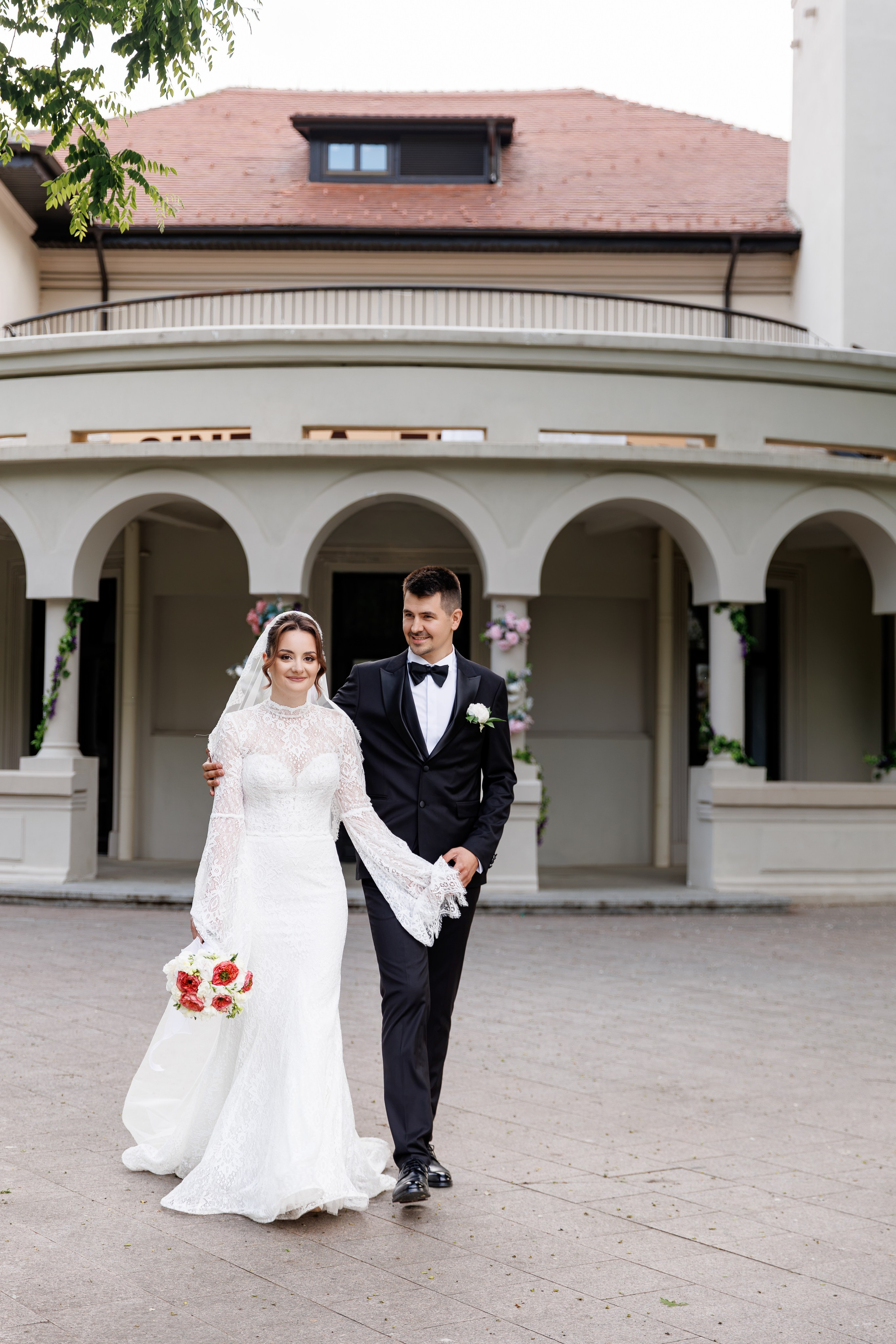 Miri plimbându-se relaxați în timpul ședinței foto de nuntă, în faăa unei clădiri elegante.
