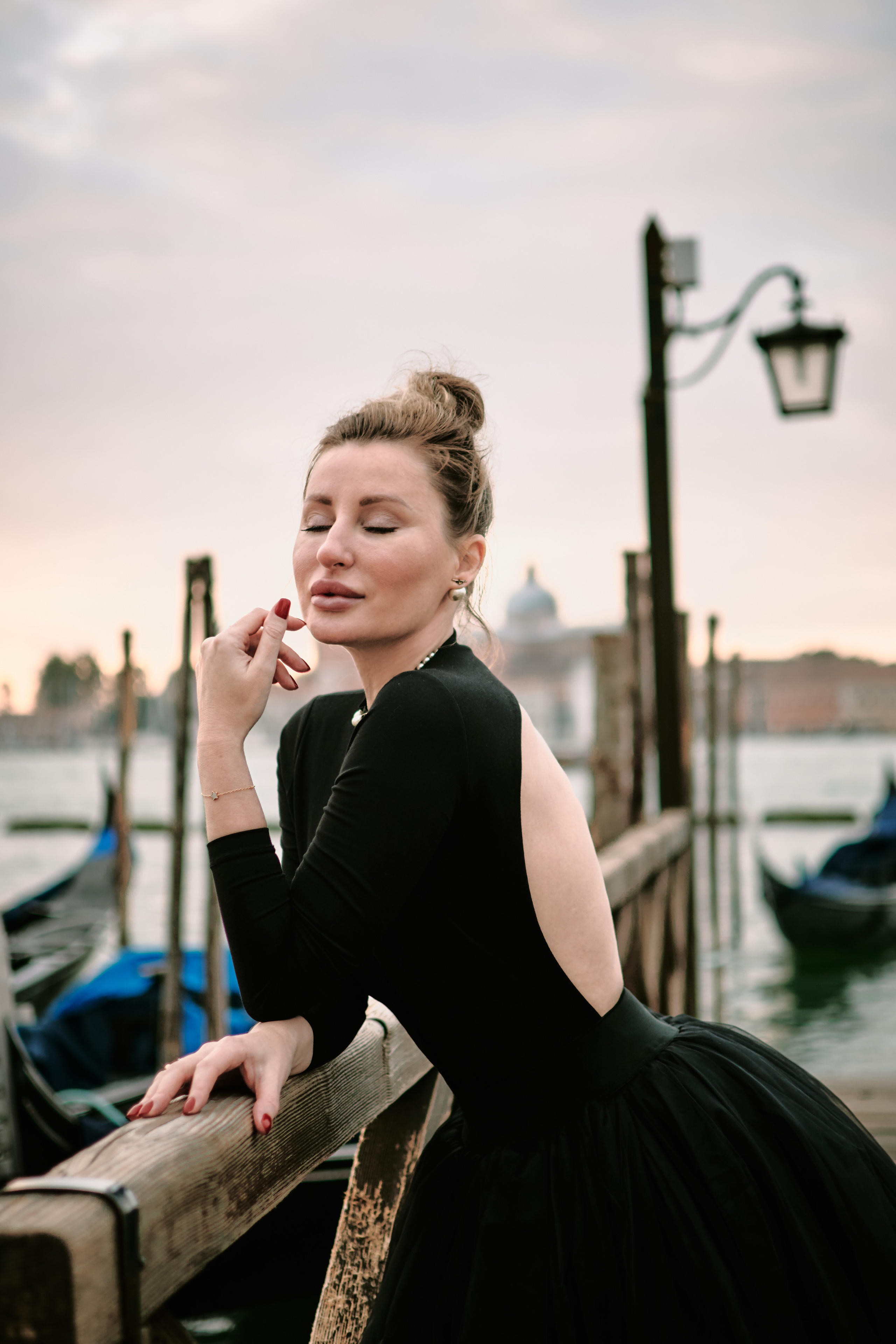 A young woman with a bright smile stands on San Marco square in Venice. She wears a flowing yellow sundress that complements the warm sunlight reflecting off the water behind her. The red and white striped poles of a gondola rest in the background, adding to the Italian charm of the scene. She looks relaxed and carefree, enjoying the beautiful day in this timeless city. Portrait of beautiful girl, A woman on a Venetian bridge with the city's iconic canals and architecture in the background