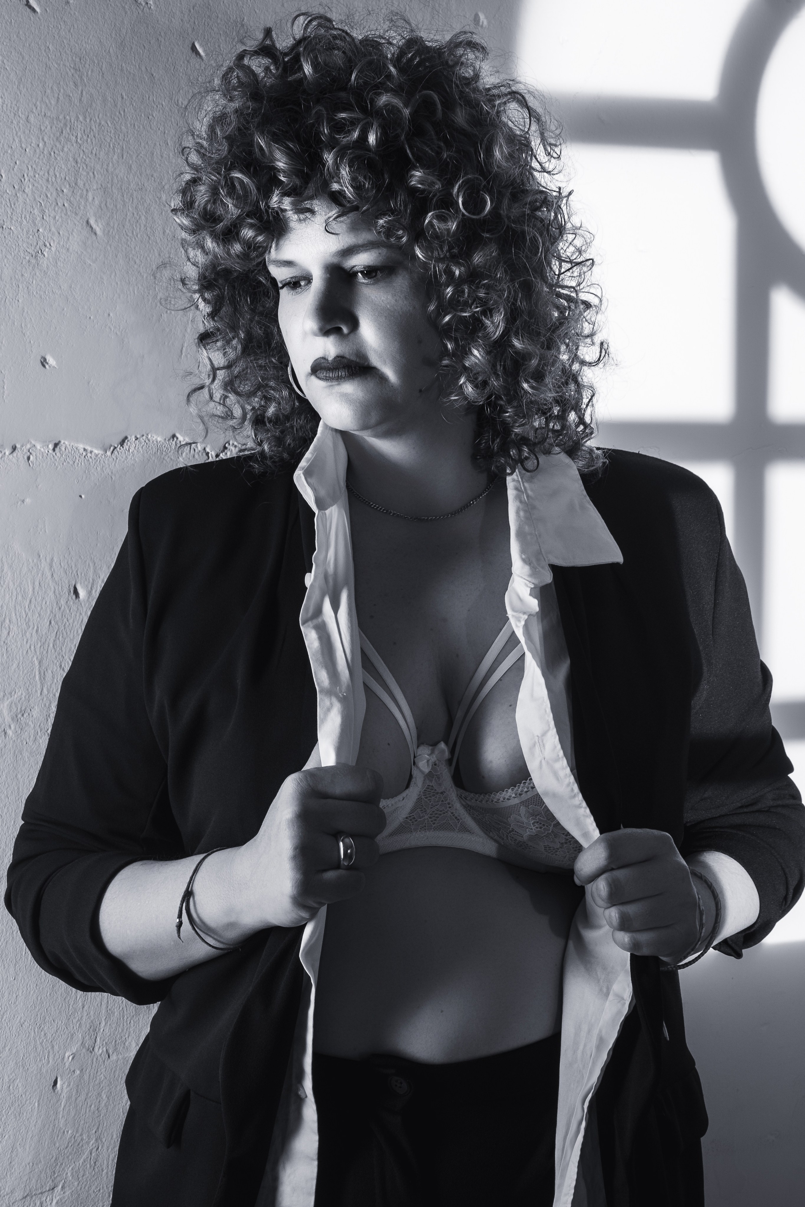 Retrato en blanco y negro de mujer con melena rizada y chaqueta negra abierta junto a la ventana