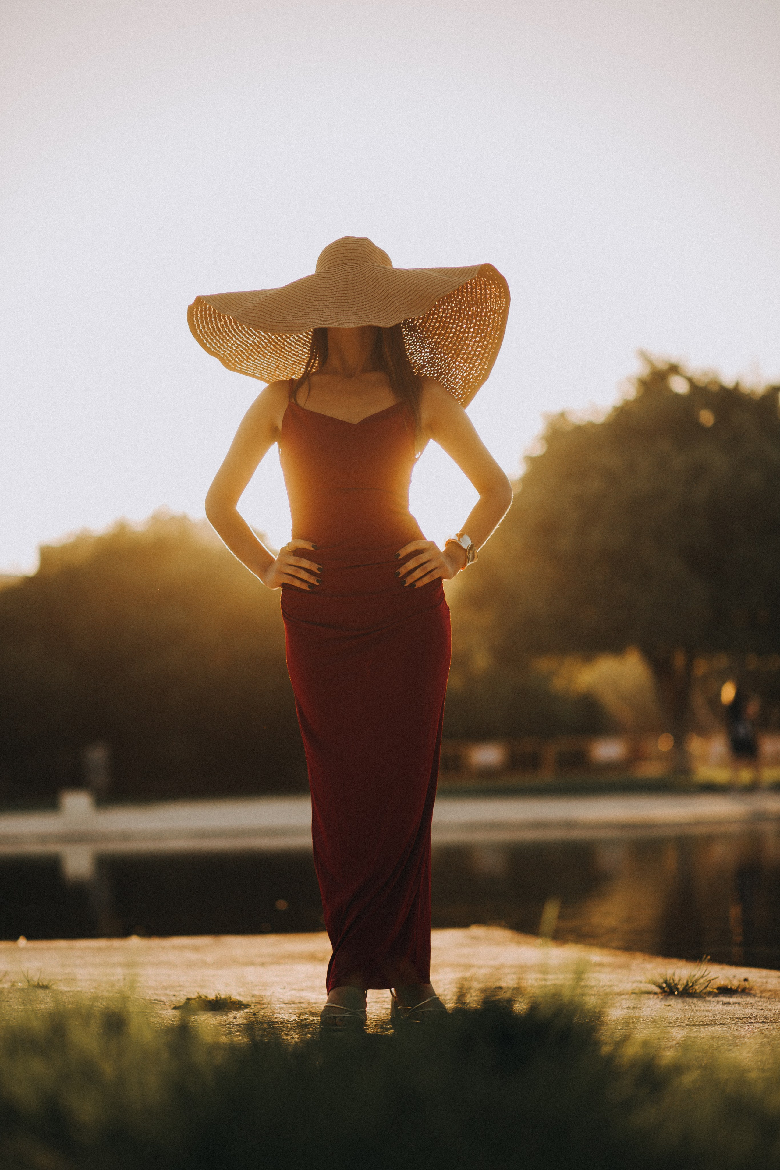 Retrato individual con estilo de una mujer con vestido rojo y sombrero de ala ancha, posando con confianza al atardecer junto al agua — un momento de hora dorada de una sesión individual en Valencia, España.