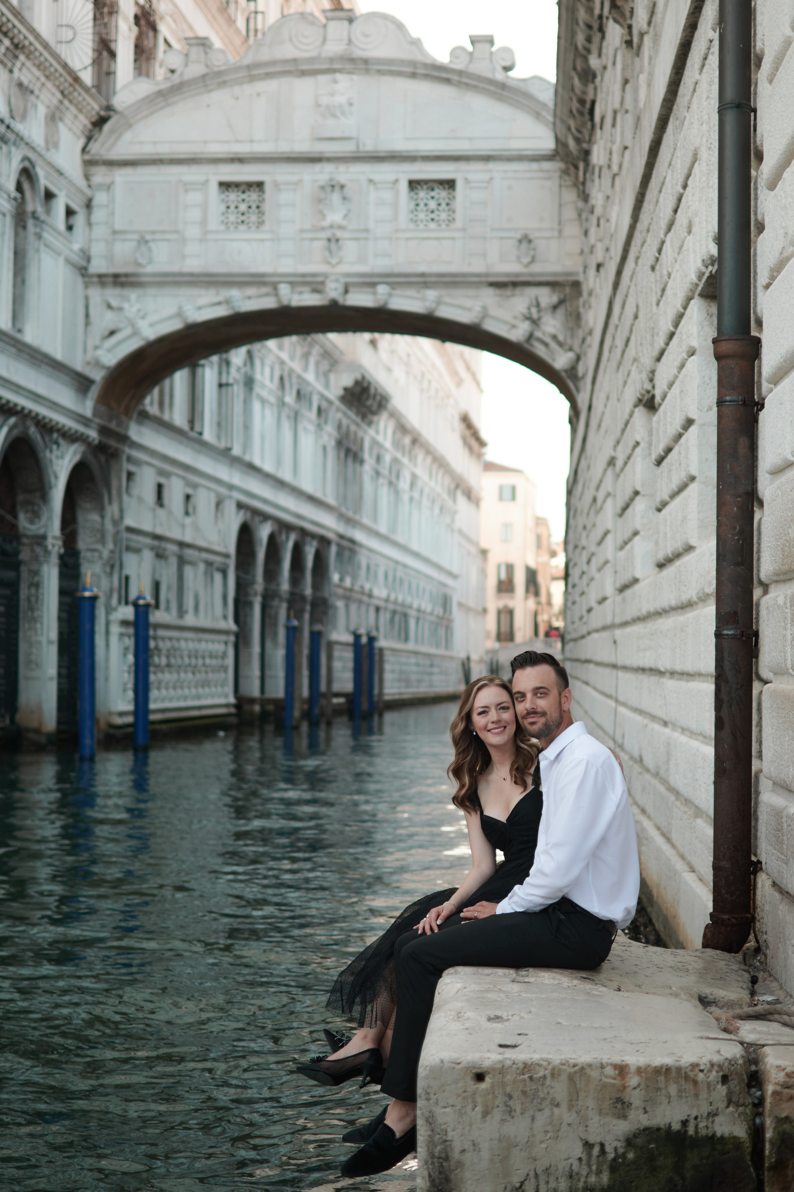 This portrait captures the timeless elegance and allure of Venice, with a young woman in a flowing blue dress standing on a narrow bridge overlooking the canal below. The intricate stonework of the bridge's arches creates a unique frame within the photo, drawing the viewer's eye to the woman's captivating presence. Bridge of Sighs in background. If you want to capture a unique angle of this iconic bridge, head to the small corner below it. This spot offers a different perspective of the Bridge of Sighs, and you can also capture the gondolas passing underneath the bridge. Italy