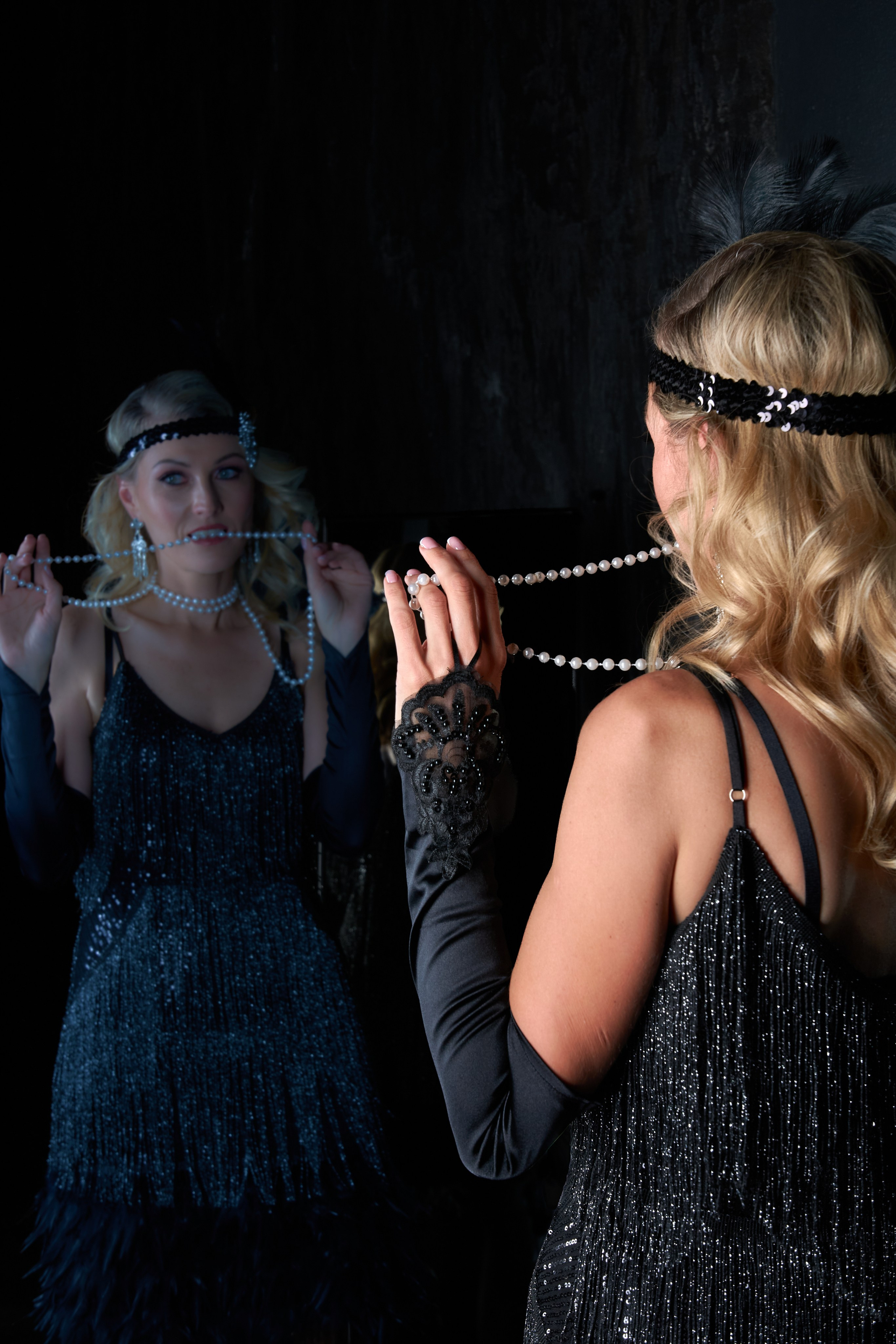 A woman and her reflection hold a string of pearls — a playful moment with her own image