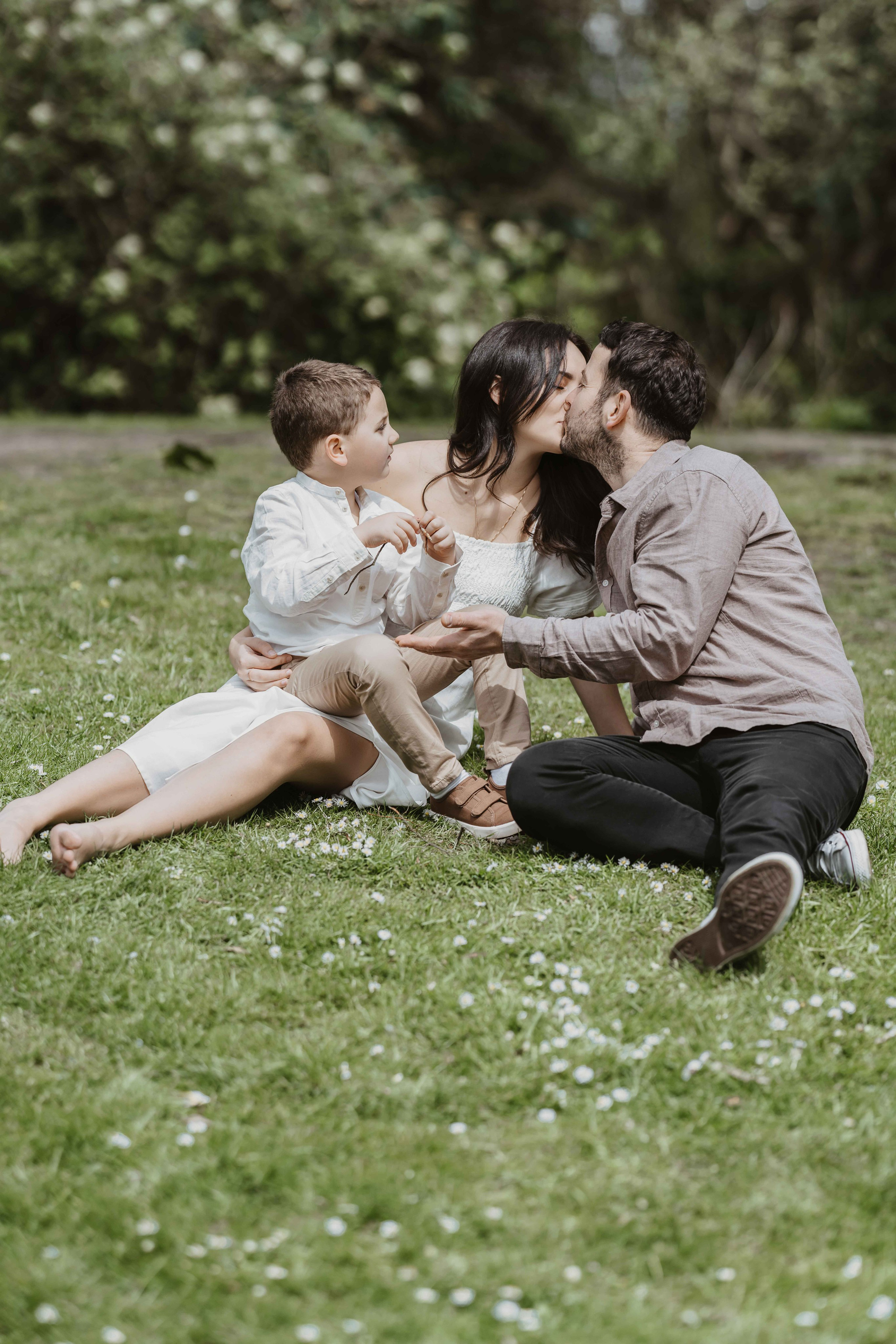 Family photoshoot in London park with parents and child sitting on grass in coordinated neutral outfits.