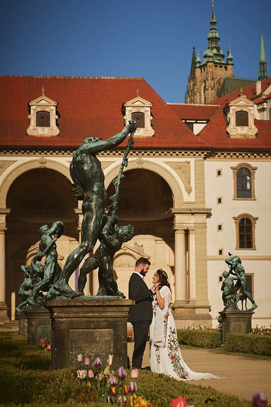 A stylish American couple sits underneath the Astronomical Clock as the bride happily shows off her engagement ring.