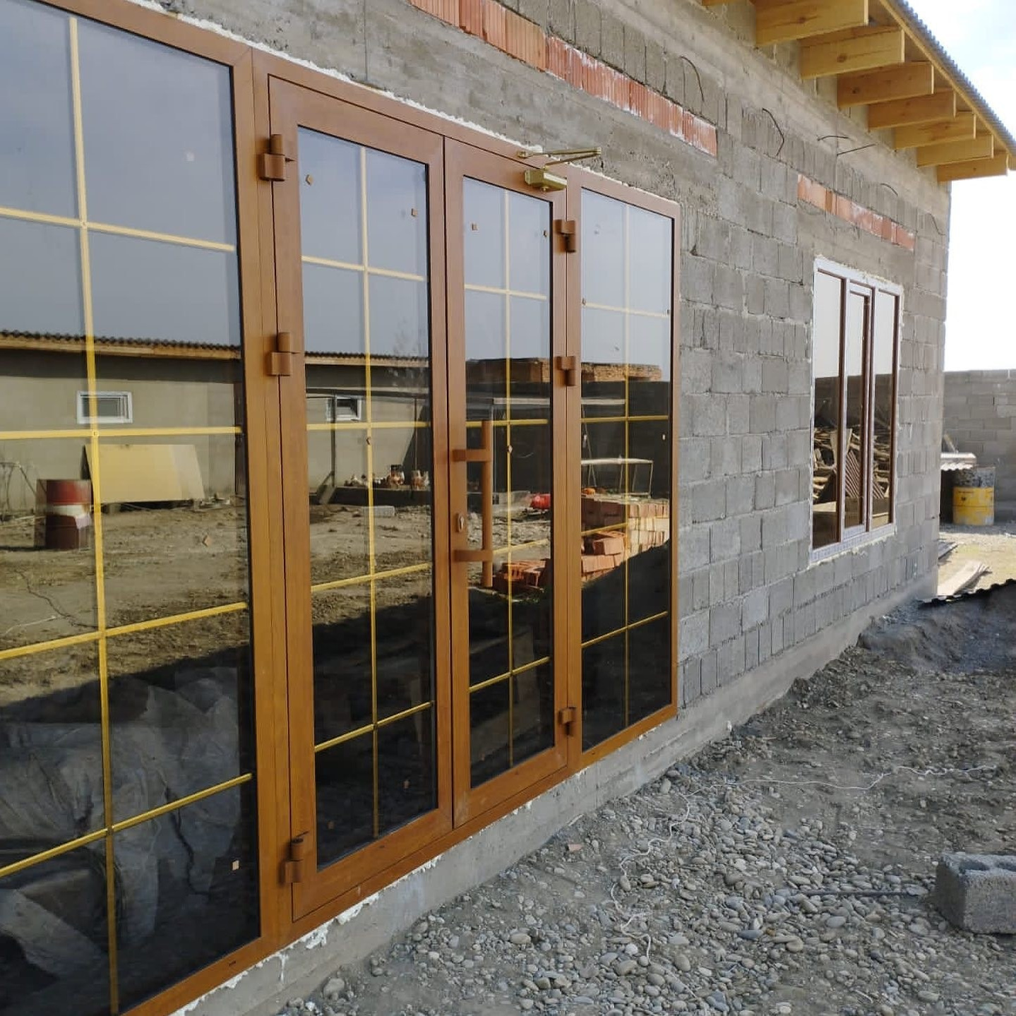 Пластиковая дверь входной группы, вместе с панорамными окнами в ламинации, тонированными стеклопакетами и шпроссами в недостроенном доме.