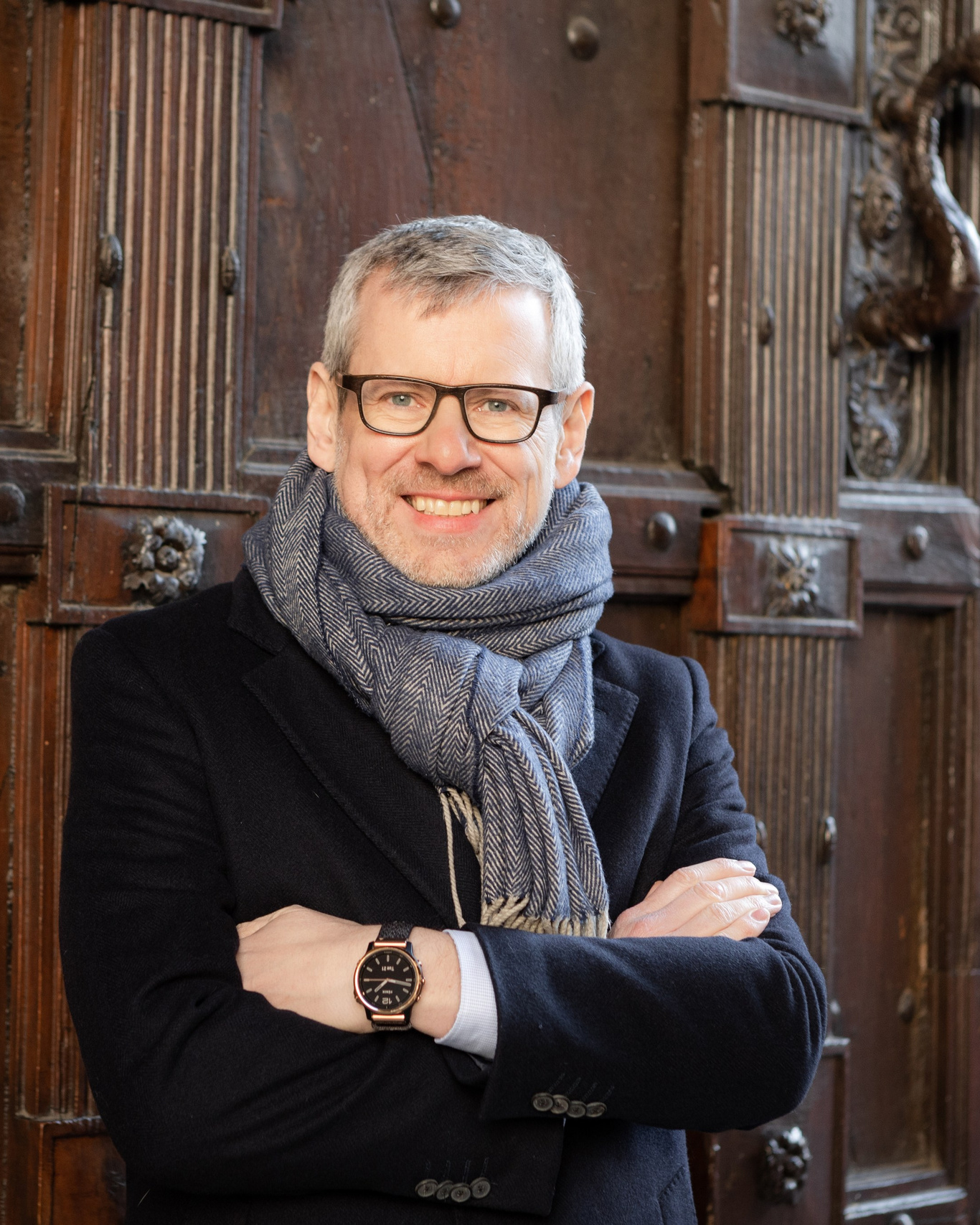 Founder with glasses in black knit and scarf against a wooden door, autumn brand portrait Toulouse