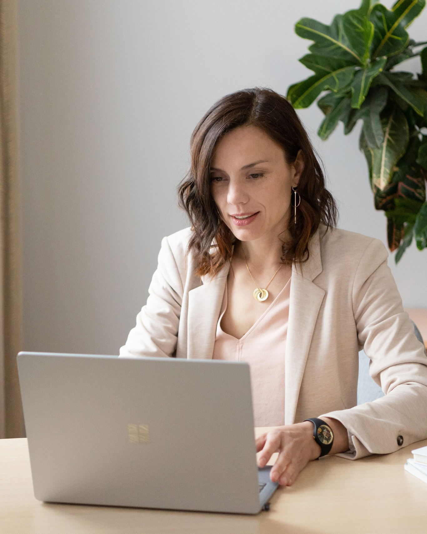 professional portrait of a woman in a light blazer using a laptop at a desk