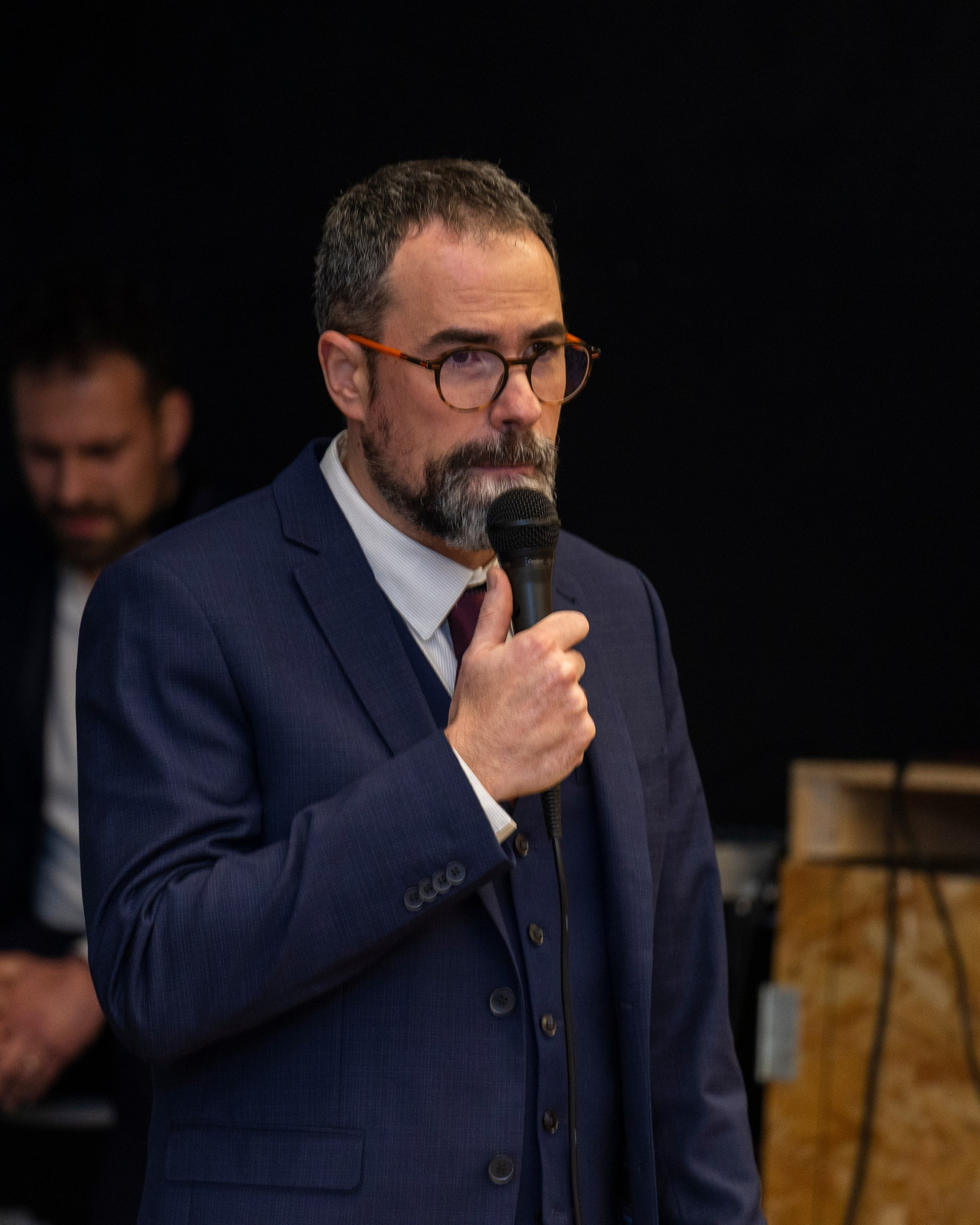 man in a suit speaking into a microphone during a corporate event