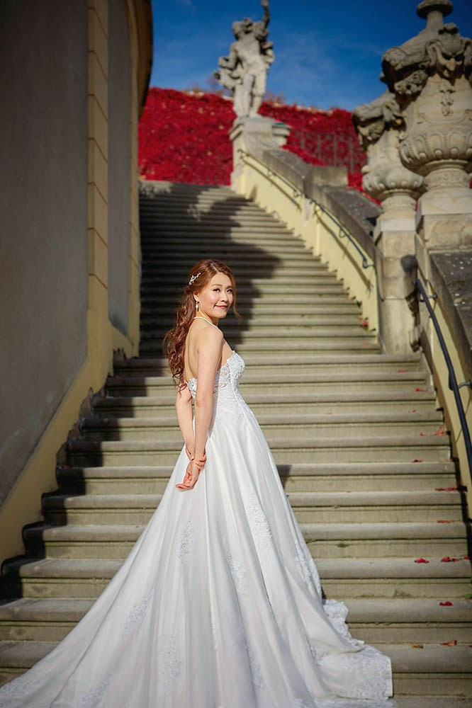 Bride looking over her shoulder, framed by statues in the Vrtba Garden.