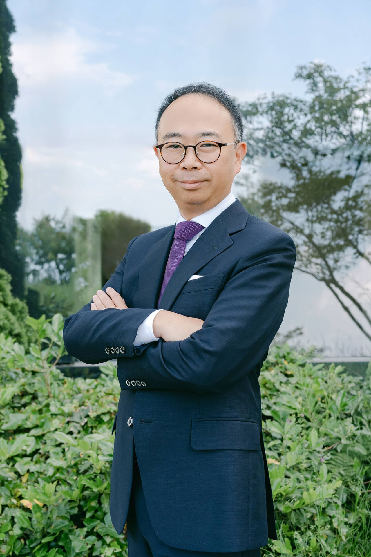 Outdoor-Corporate-Porträt eines Mannes mit verschränkten Armen vor Grün (nahbares Leadership-Bild)