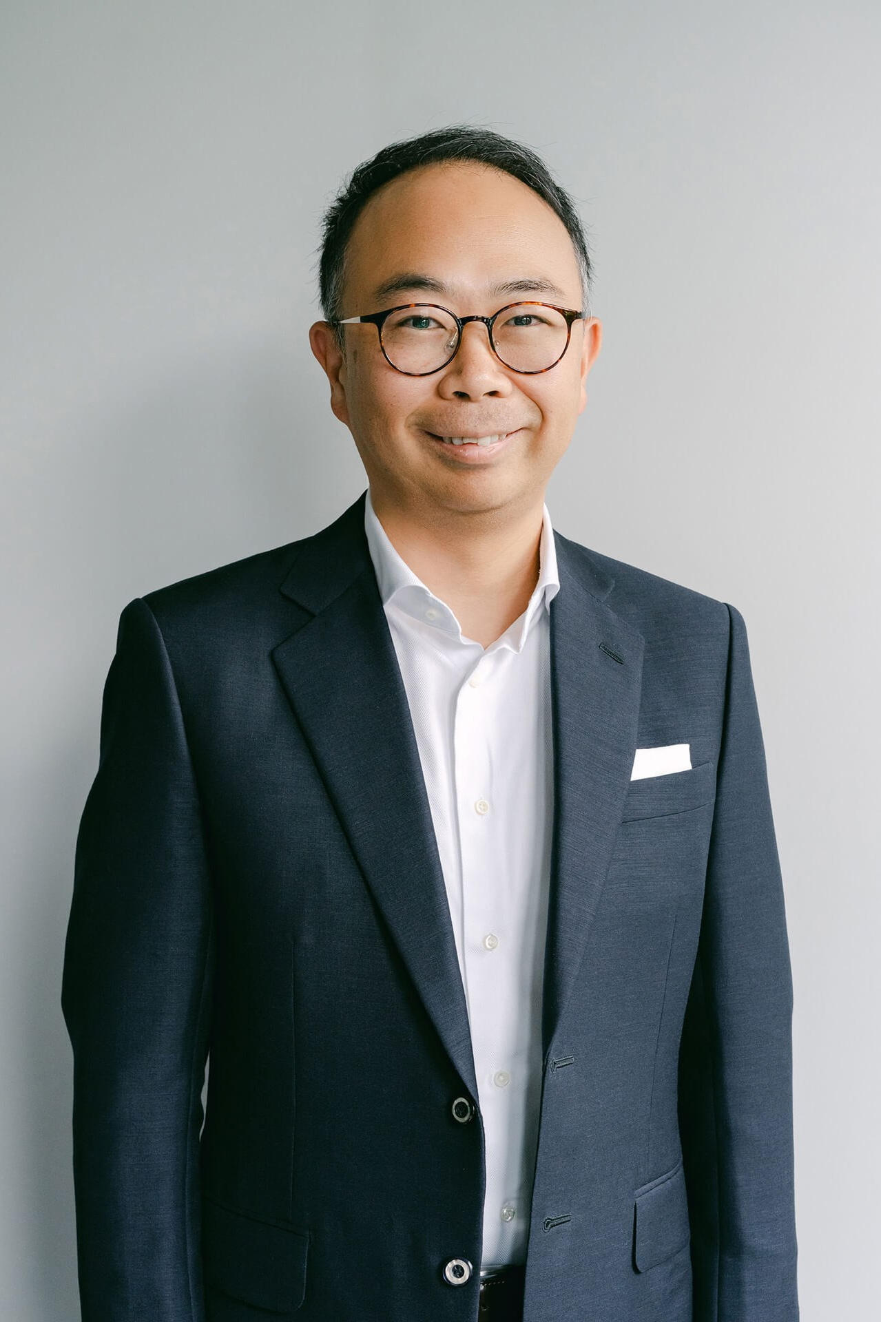 Business-Headshot eines Mannes im dunkelblauen Anzug vor neutralem Hintergrund, selbstbewusstes Lächeln