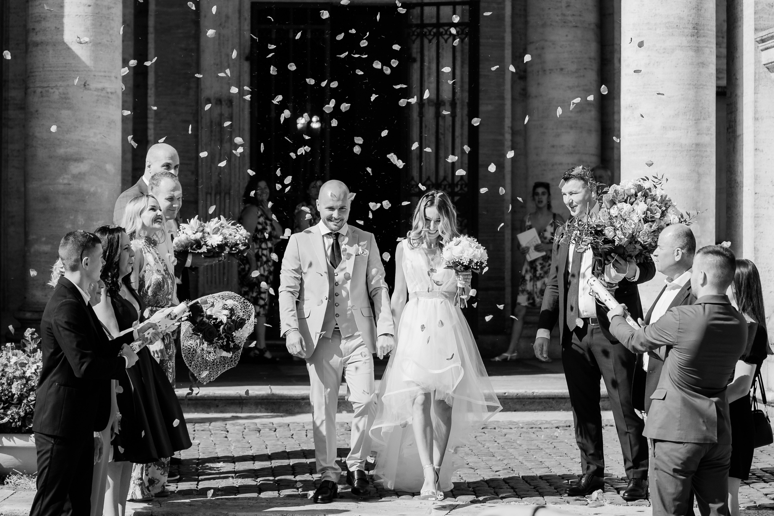 Neosposi al rito civile tra gli applausi, con gli invitati che lanciano petali, catturati in una fotografia in bianco e nero che cattura la gioia e l'euforia del momento.
