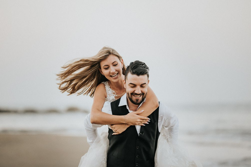 Una coppia di sposi si abbraccia in un ballo romantico sulla riva del mare, con l'orizzonte sfocato in lontananza.