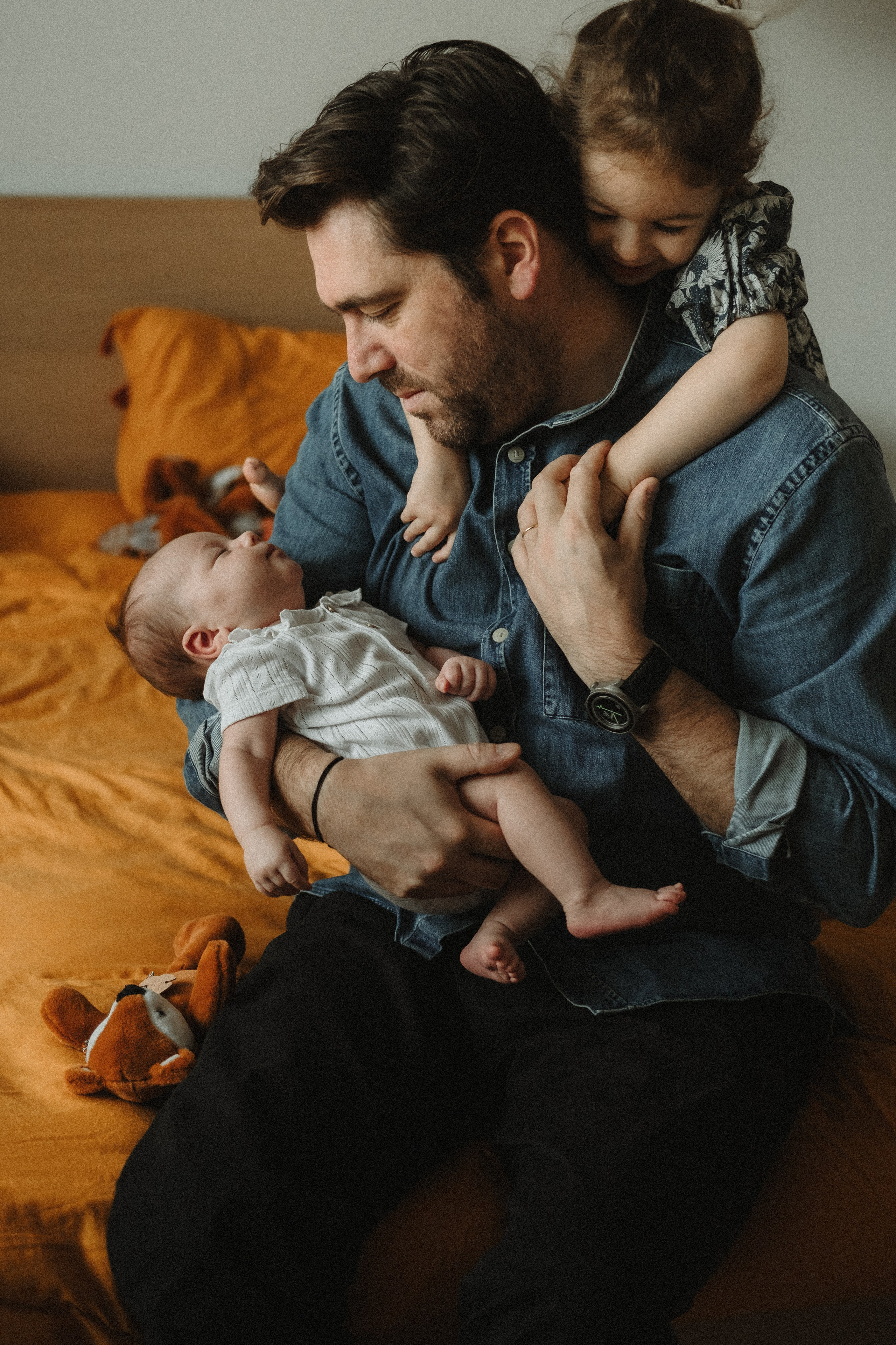 A photograph of a dad with his newborn baby and toddler daughter