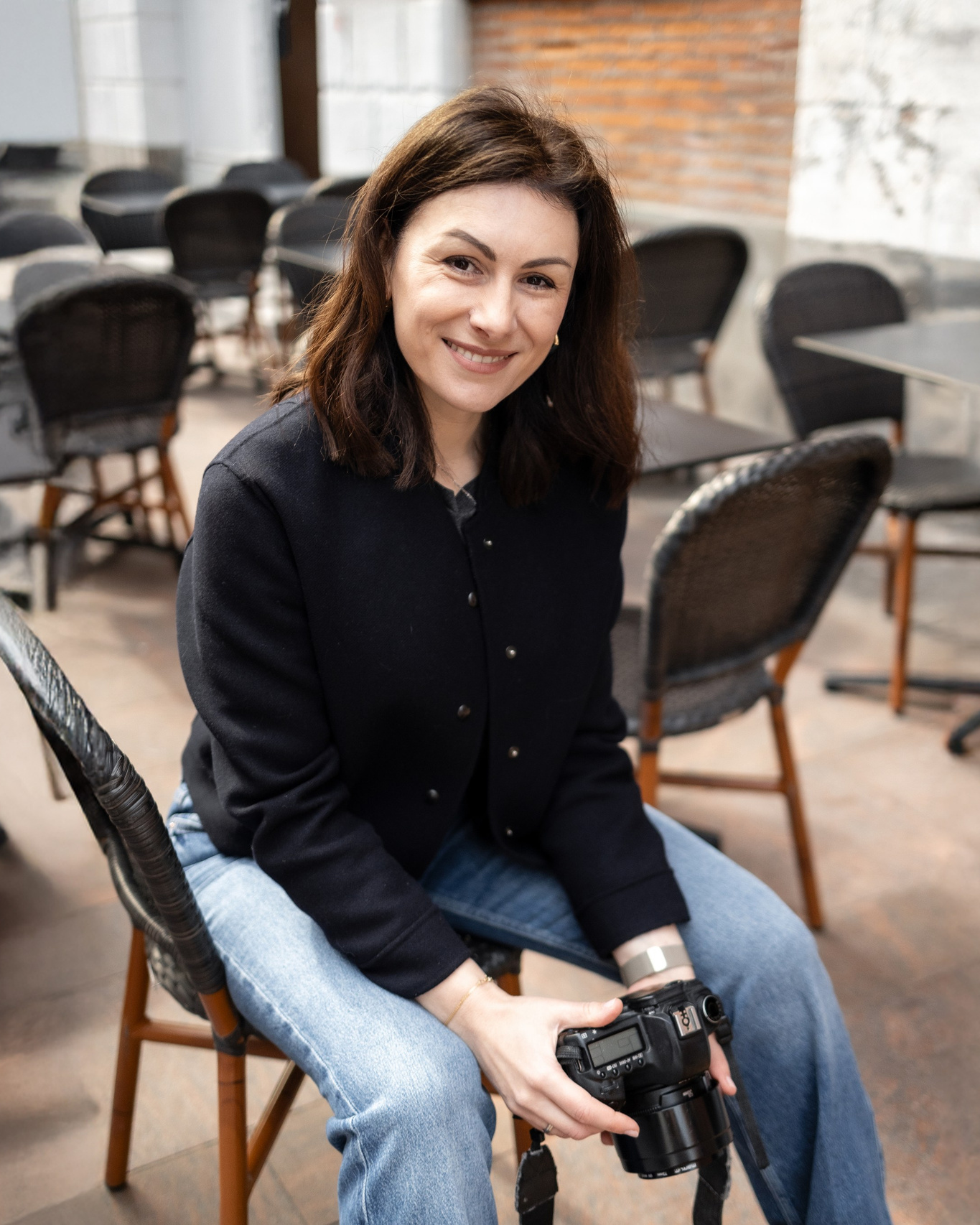 Eugénie Smirnova, photographe corporate à Toulouse, portrait assis avec appareil photo à la main, intérieur restaurant en lumière naturelle