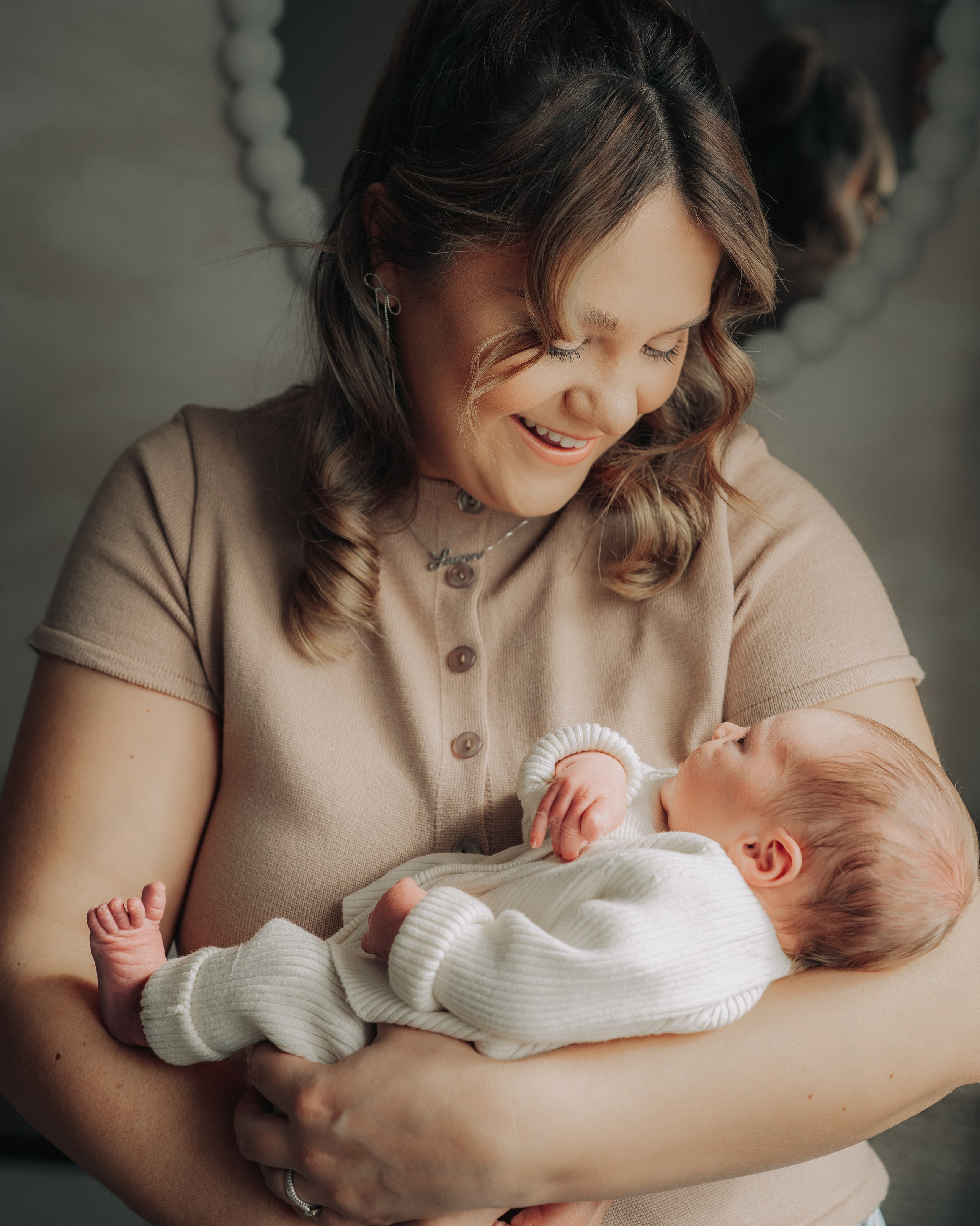 Mother in a beige sweater holding her newborn during a relaxed in-home newborn photoshoot in Newcastle upon Tyne, warm and natural moment