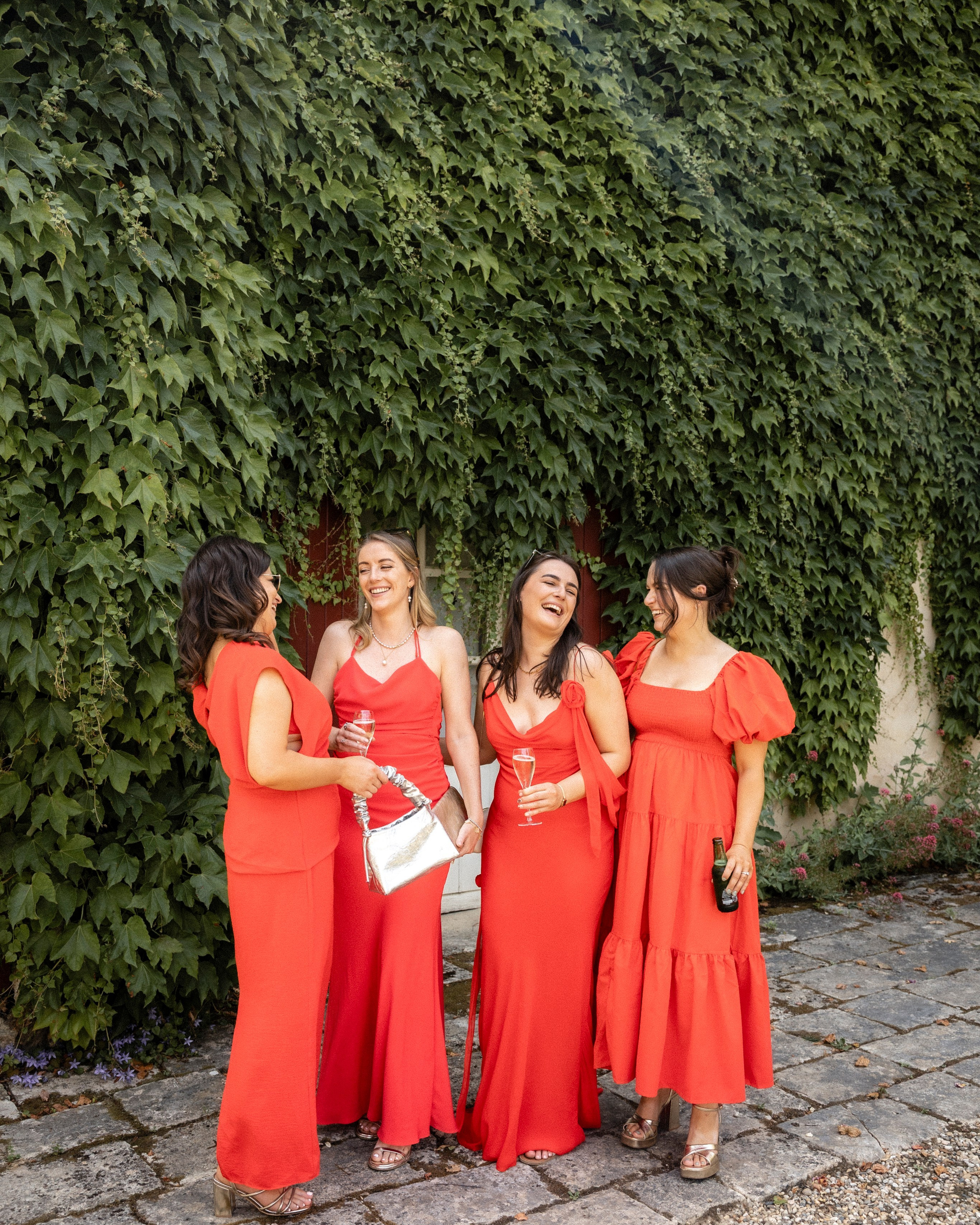 Bridesmaids in elegant red dresses laughing together during a destination wedding at Château Sentout in France.