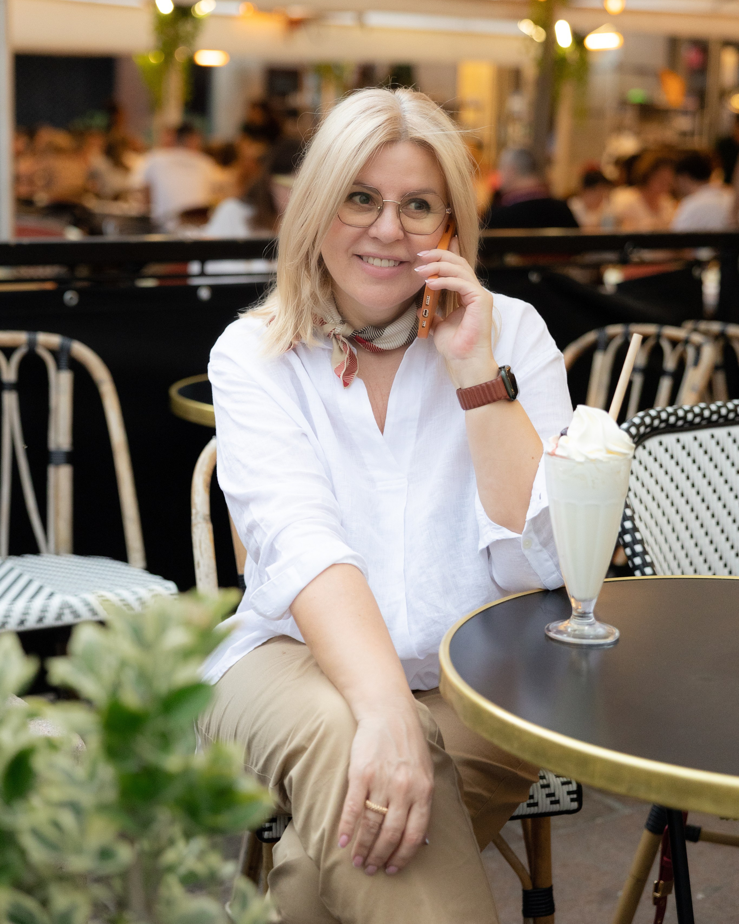 Senior founder in white shirt at an outdoor café table, refined brand portrait in golden light