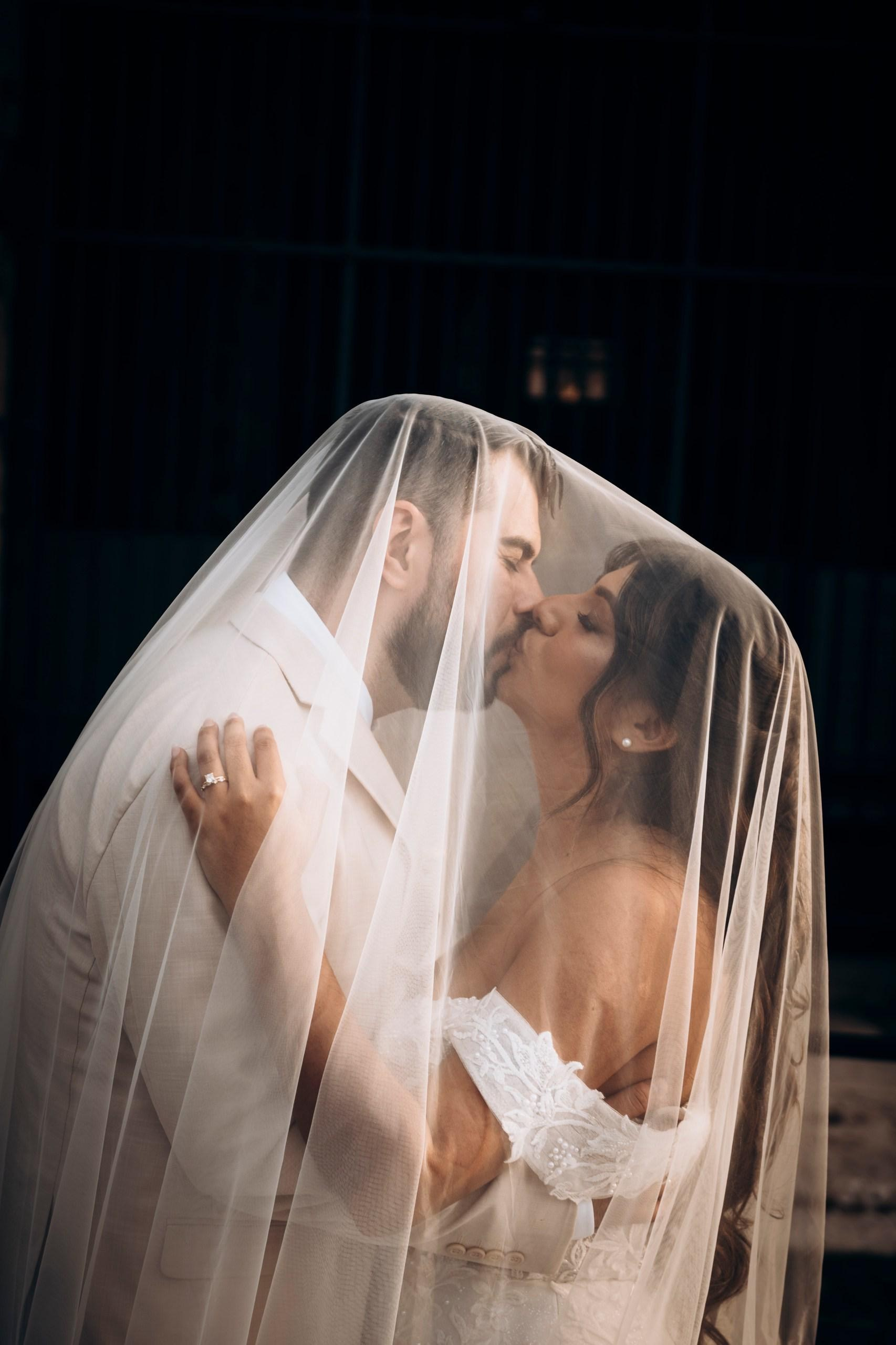 Bride and groom sharing an intimate kiss under the veil, timeless wedding moment in Italy