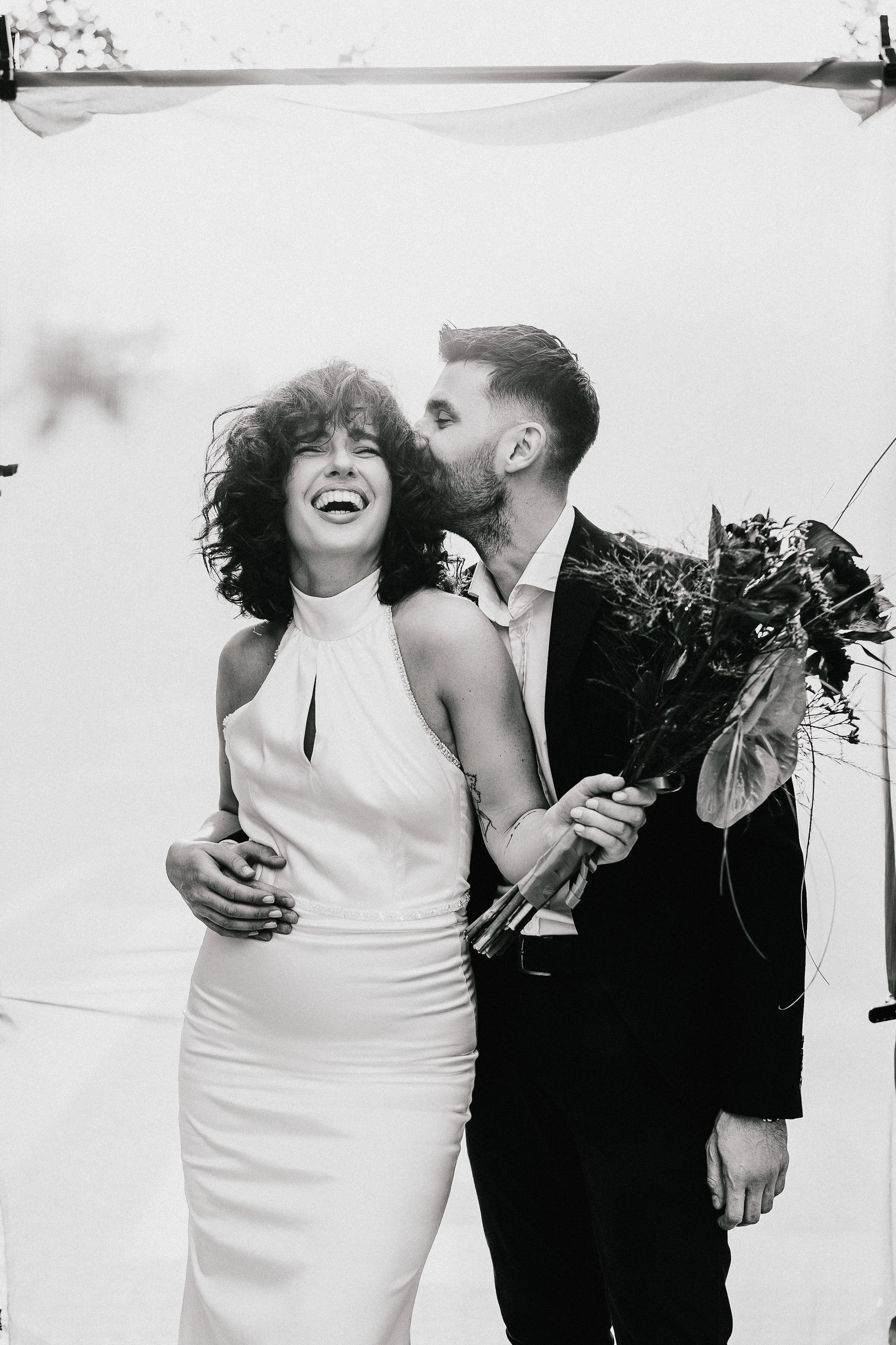 malda koja se smeje dok je mladoženja grli oko struka i ljubi