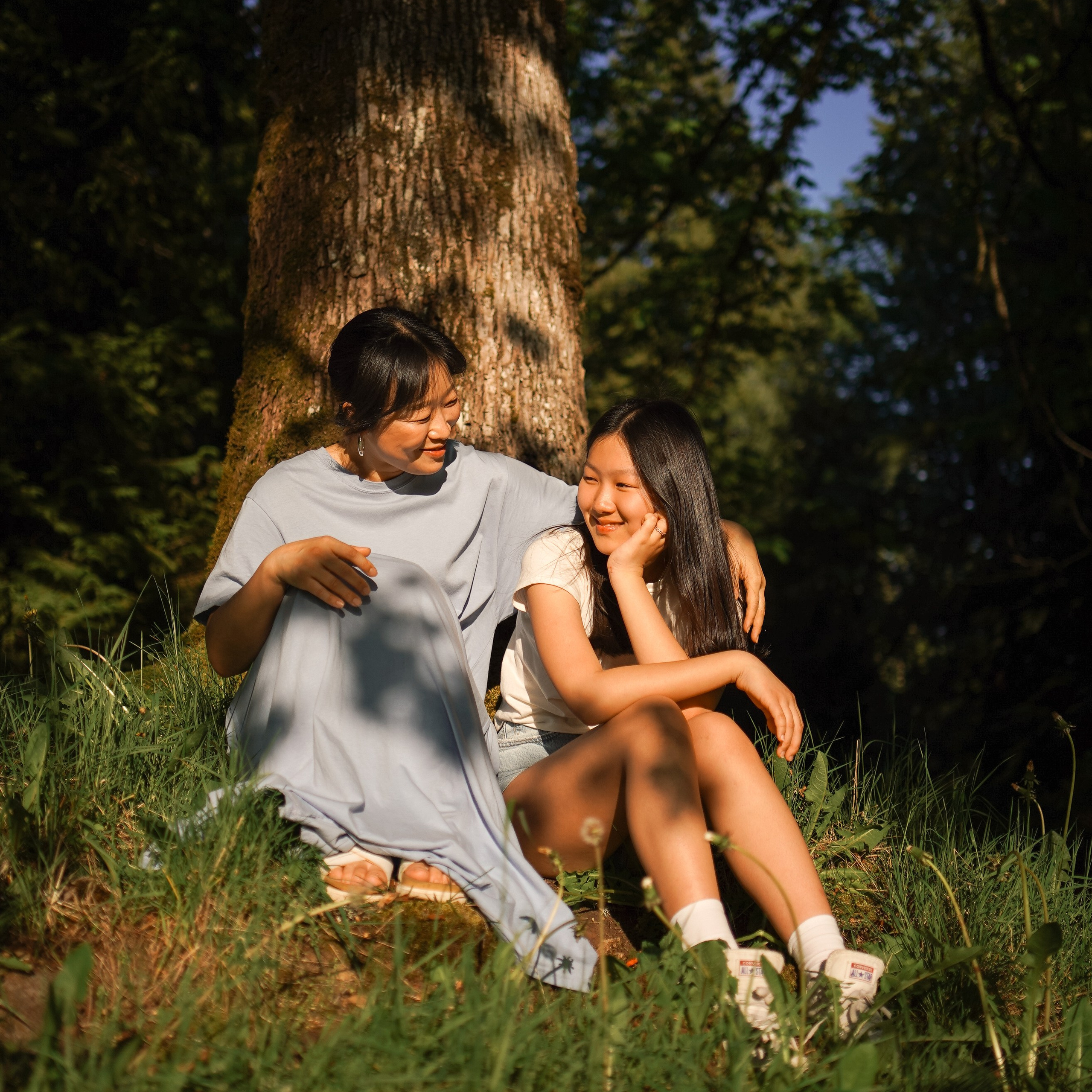 Mother and daughter sitting under a tree during golden hour in Burnaby and looking at each other with a smile