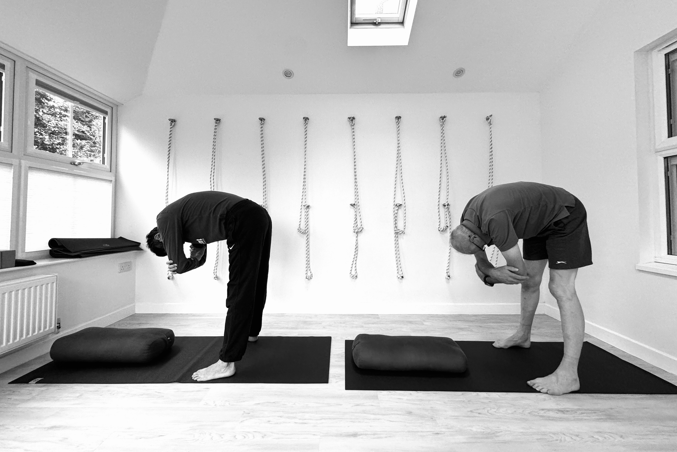 Two students practising standing forward fold in a private Iyengar yoga session in Solihull studio.