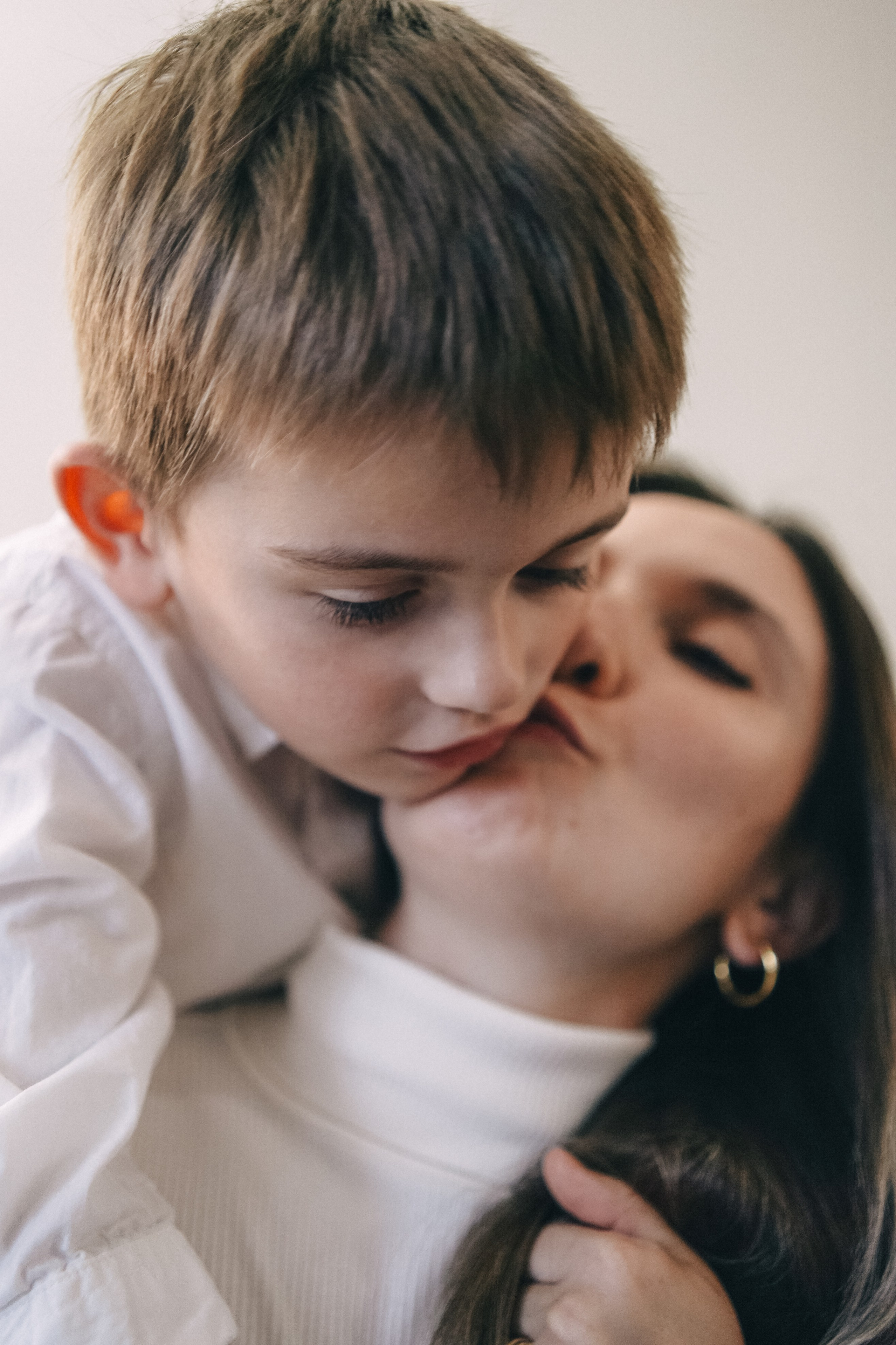 Mother is kissing her son, who is leaning on her and looking down