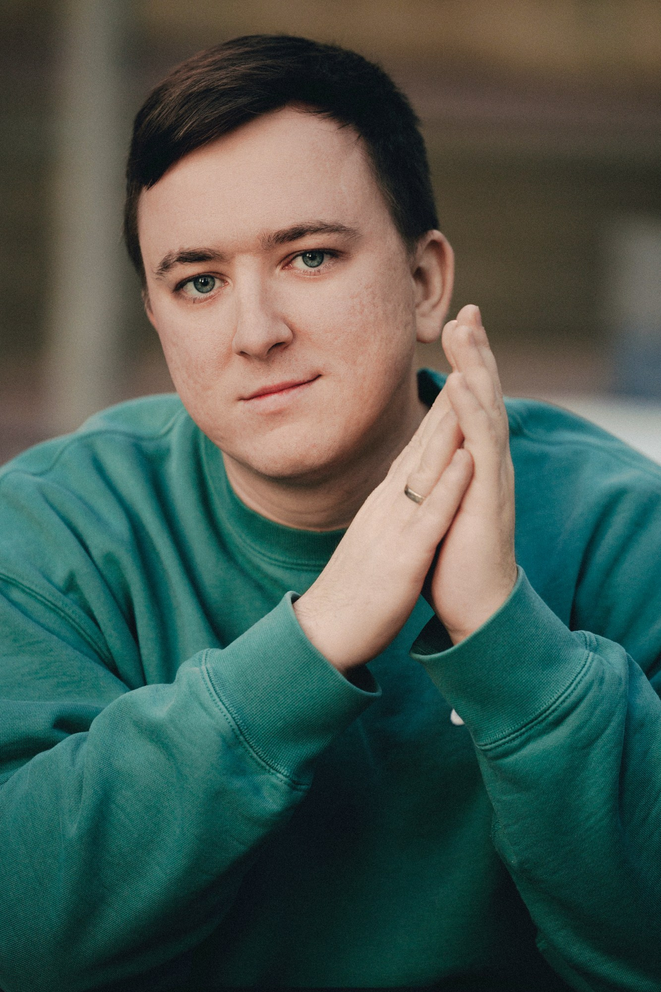 Portrait of man in green sweatshirt with hands clasped