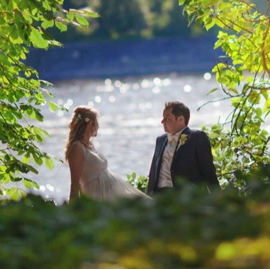 Smiling blonde-haired Swiss bride smiles lovingly towards her Italian groom as he looks towards the camera at a garden in Prague. 