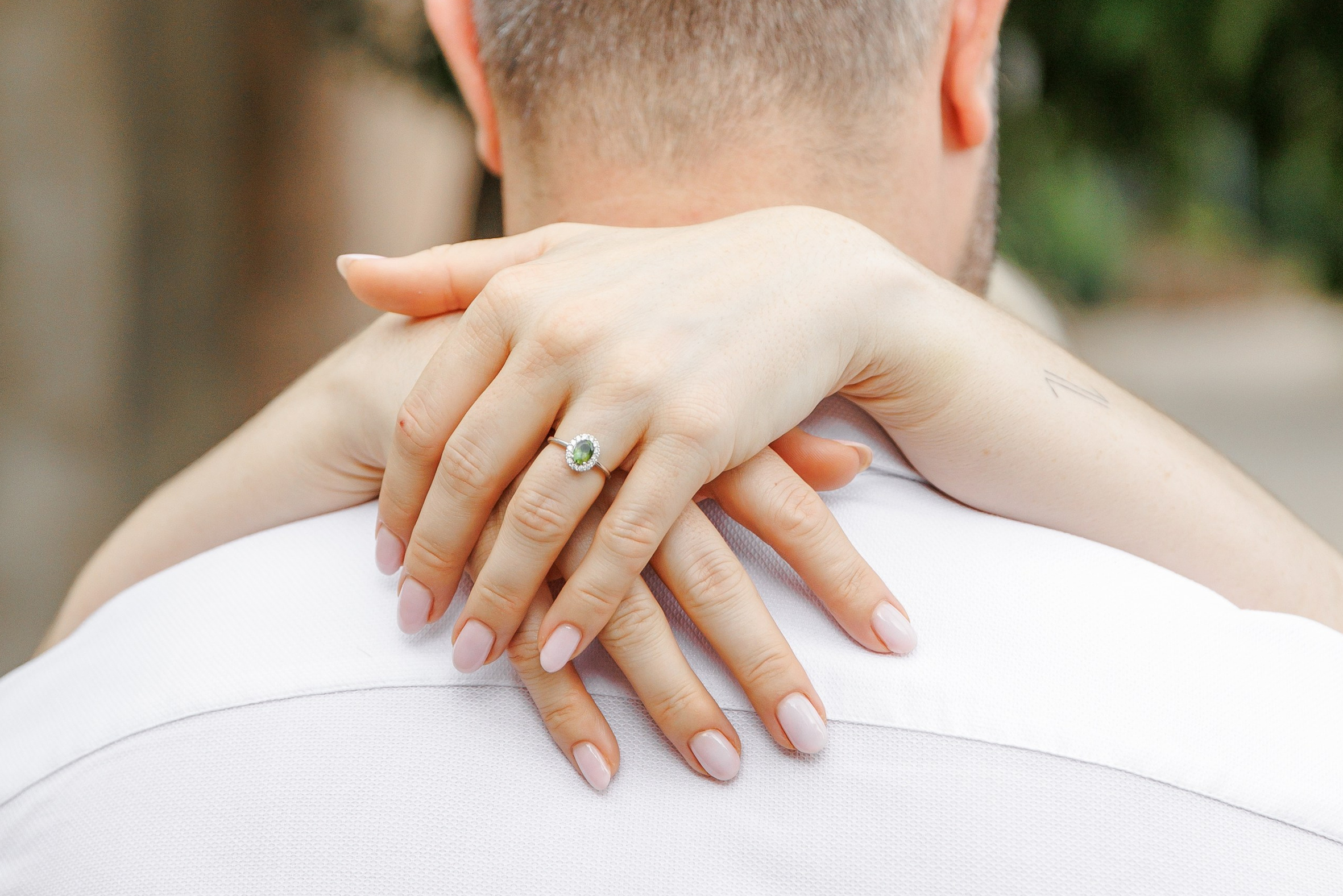 A woman holding her hands around her fiancé's back and showing the engagement ring.
