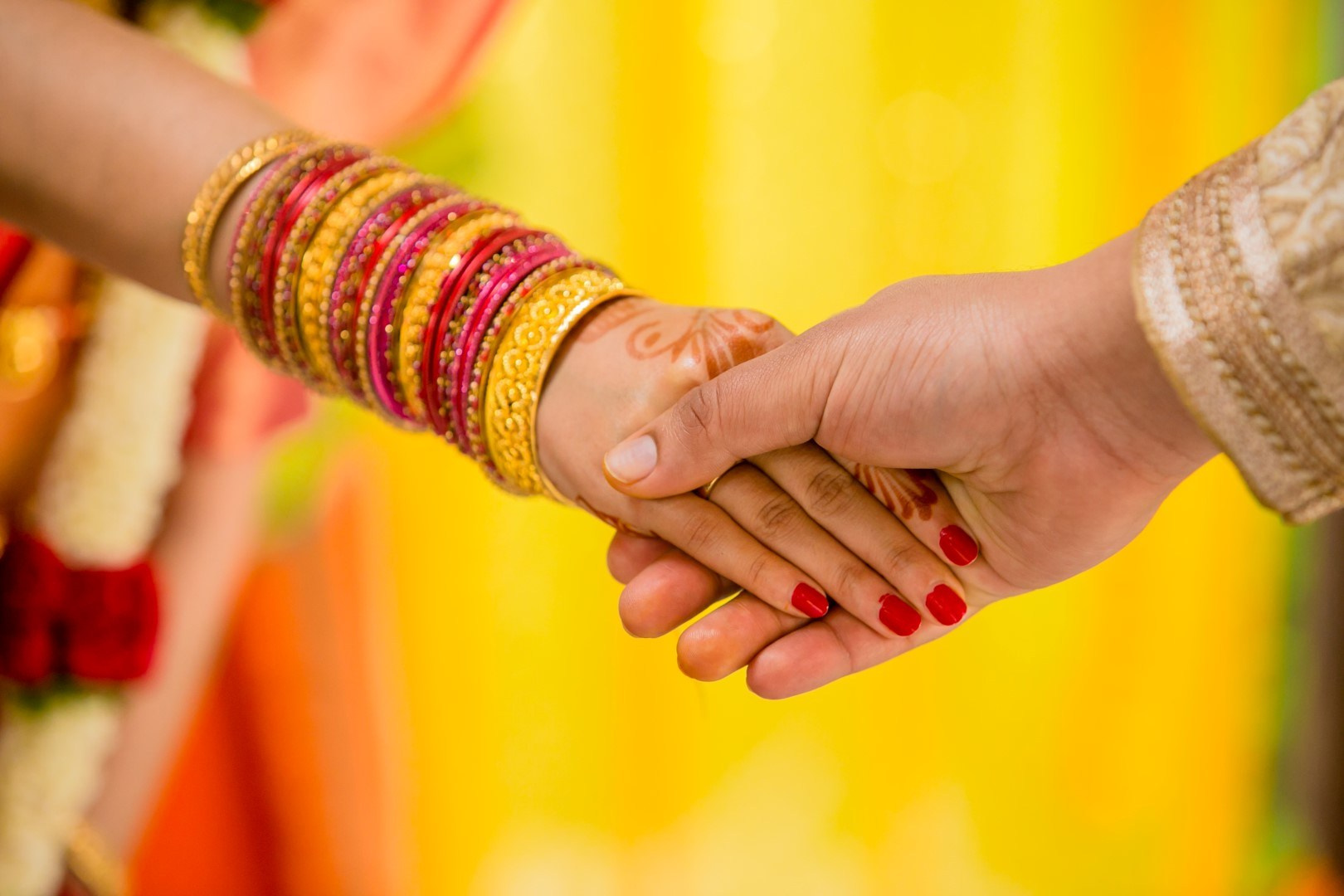 Couple holding hands, bangles against a yellow backdrop, Indian wedding detail