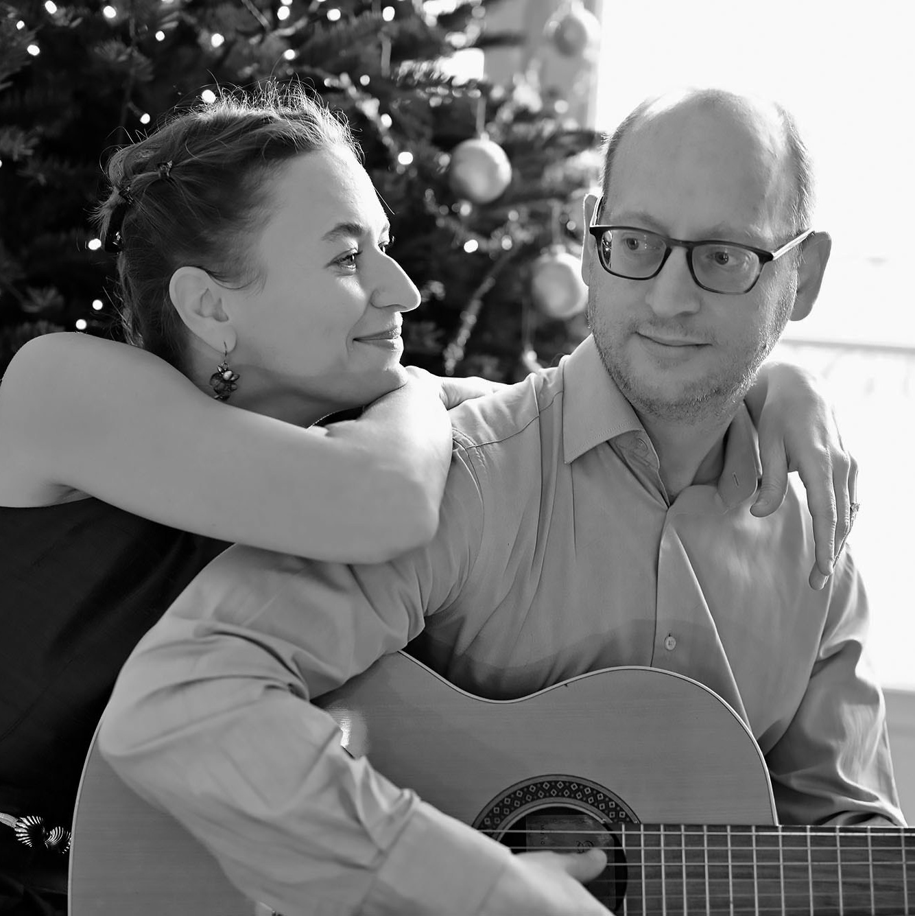 Женщина и мужчина сидят у окна . Мужчина держит в руках гитару и играет для своей женщины 